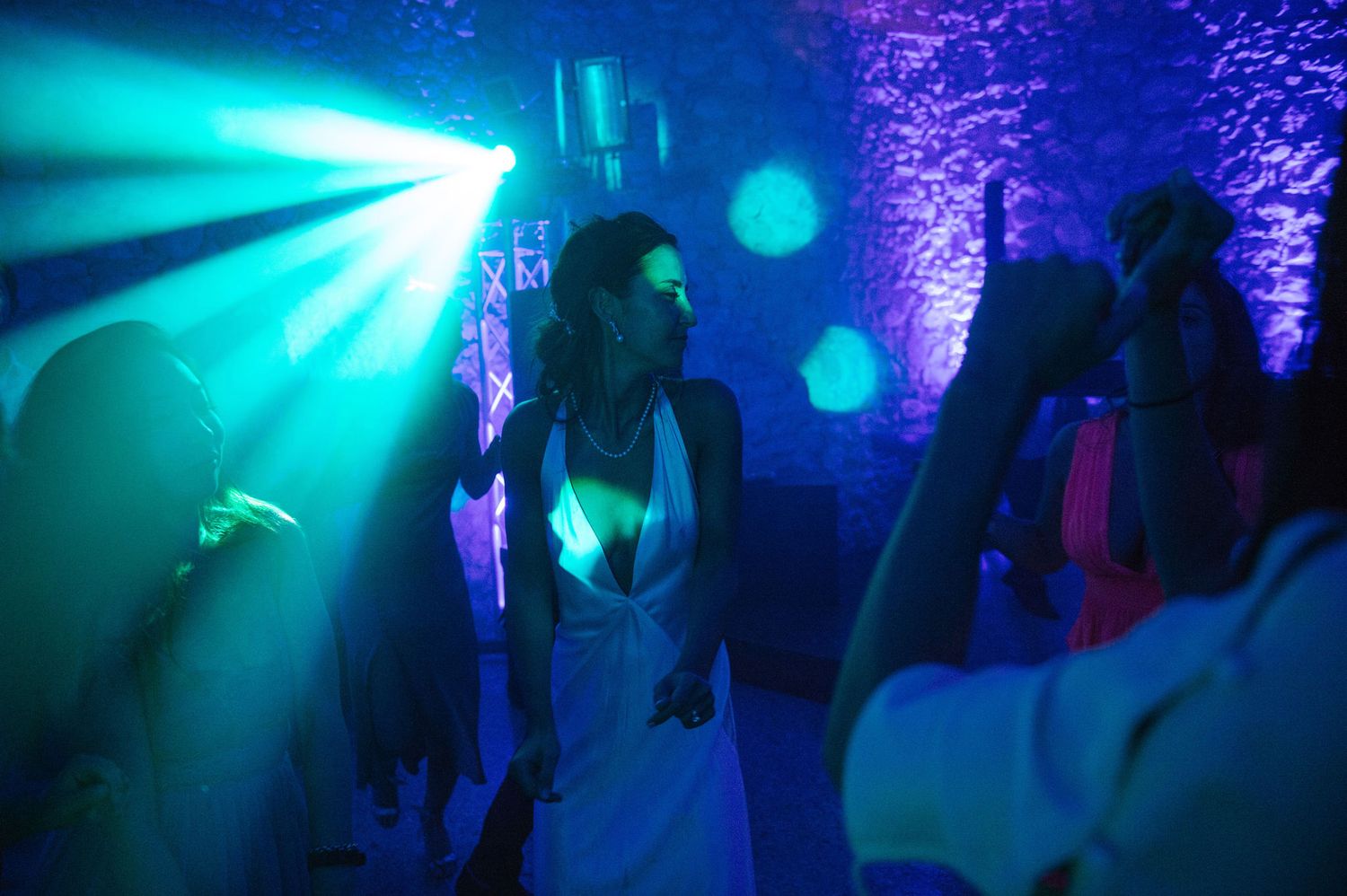 Dance floor illuminated by vibrant teal spotlights and fog effects at a wedding reception.
