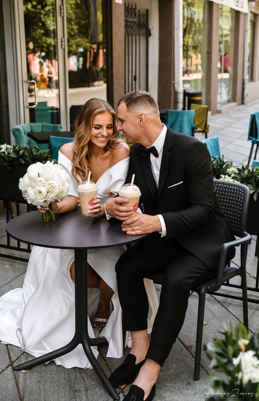 Newlyweds sharing intimate moments at outdoor cafe with white floral decor.