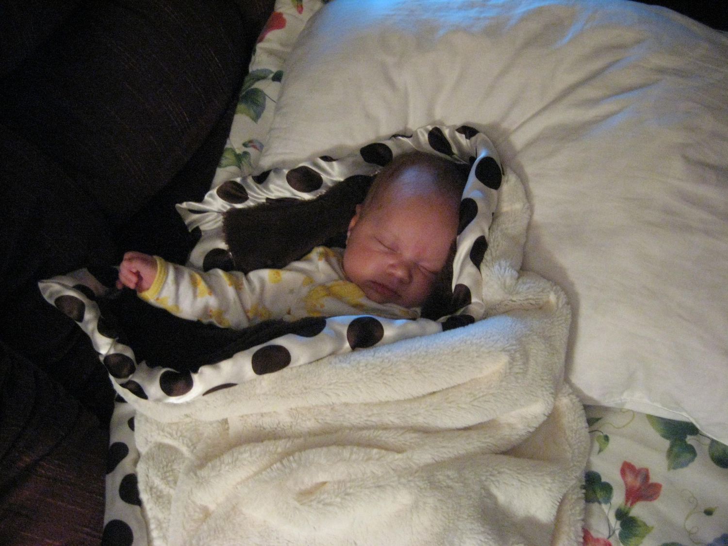 Sleeping baby wrapped in polka dot blanket on white bedding.