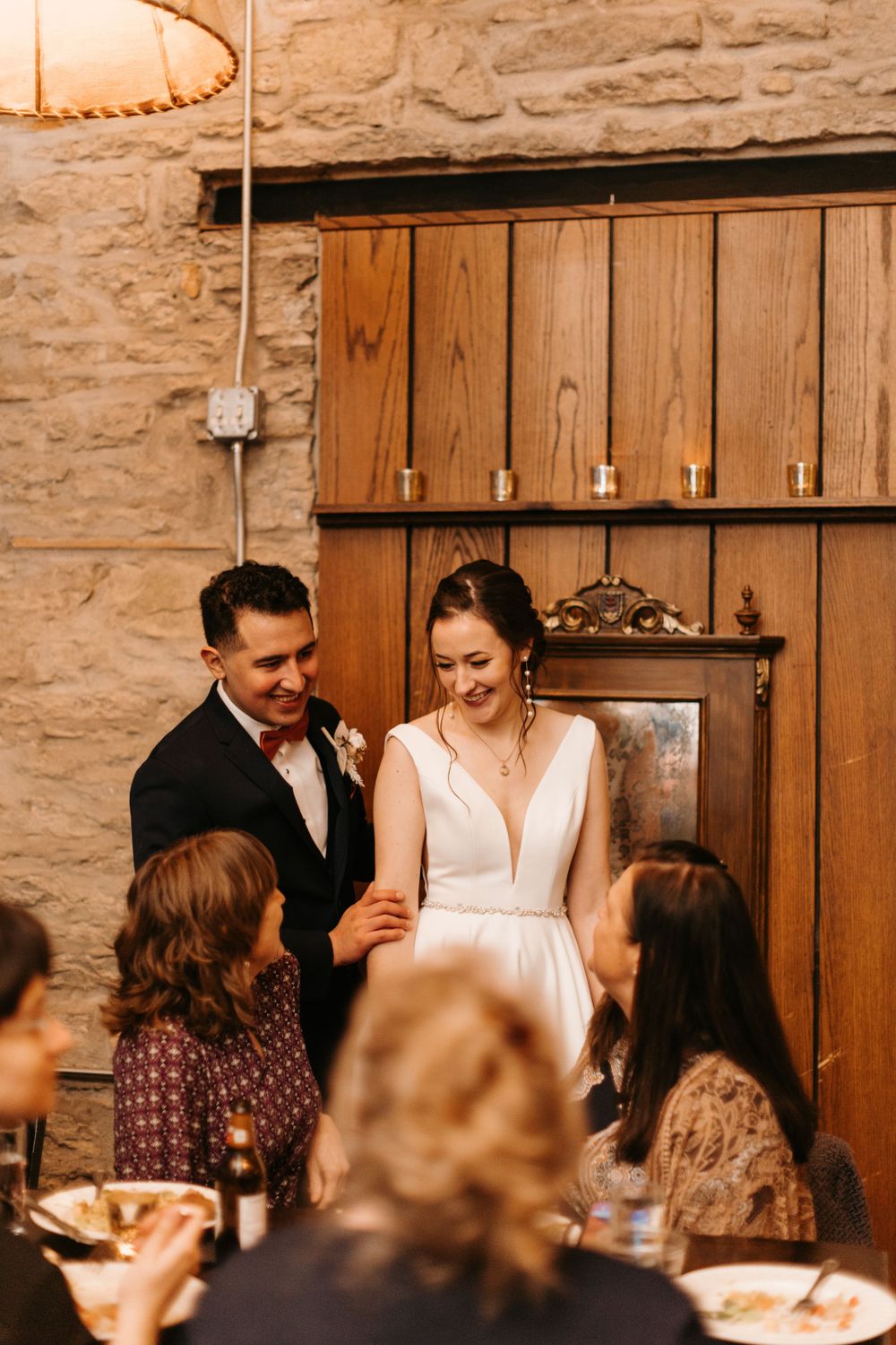 Bride and groom smiling together with guests at a candlelit rustic wedding reception.