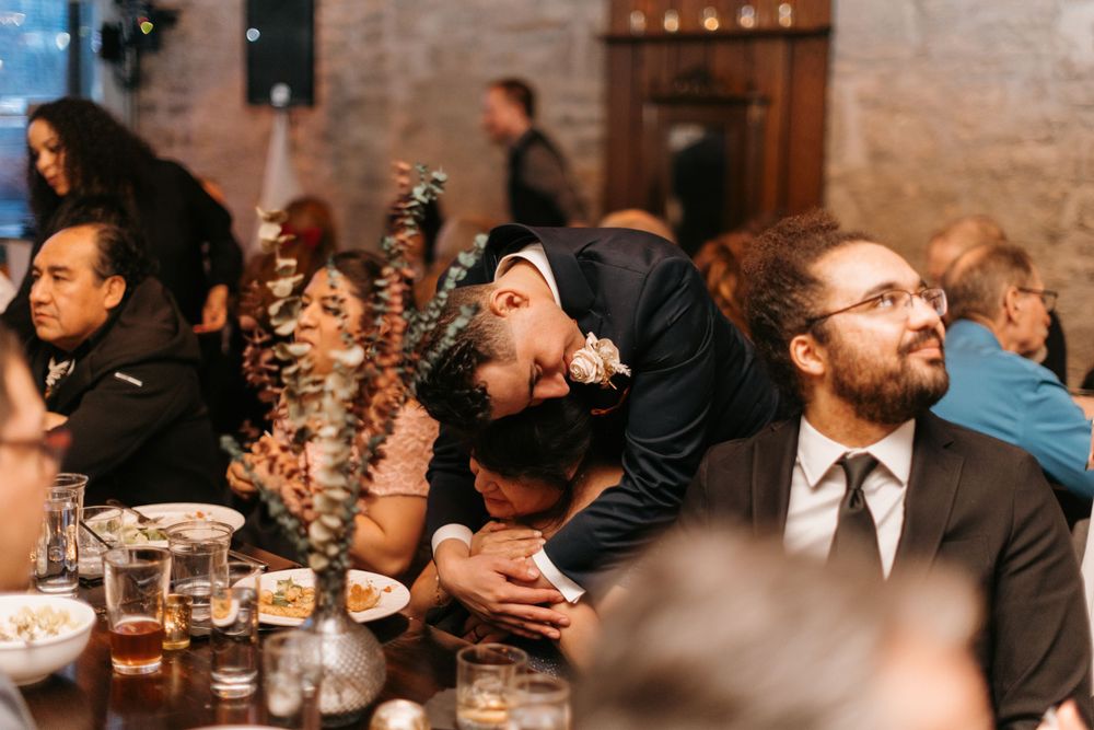 Guests laughing and embracing at a romantic wedding reception dinner in a rustic venue.