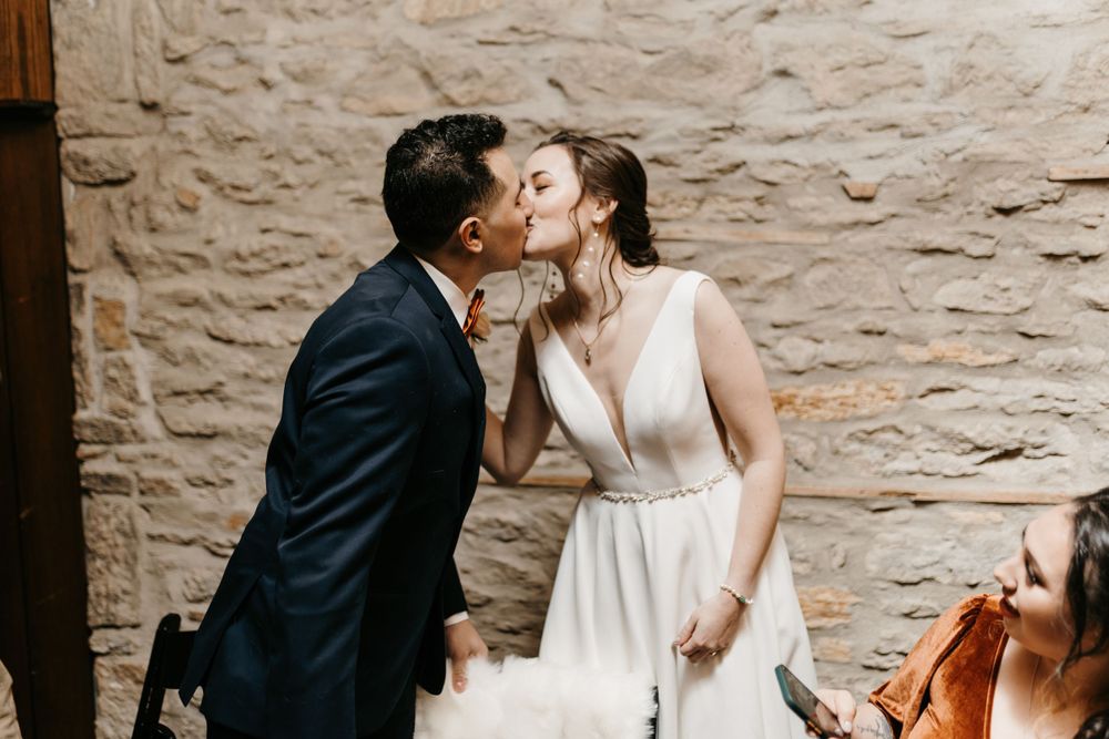 Newlyweds share a first kiss at the altar against a rustic stone wall backdrop at their wedding.