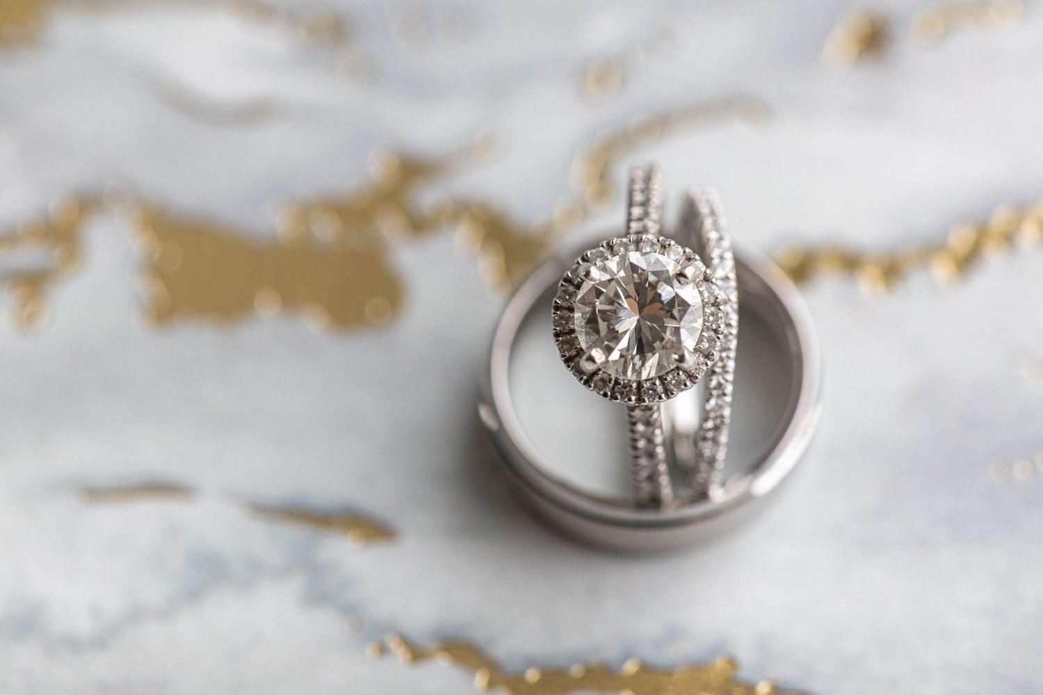 Elegant diamond halo engagement ring with wedding bands displayed on a marble surface.