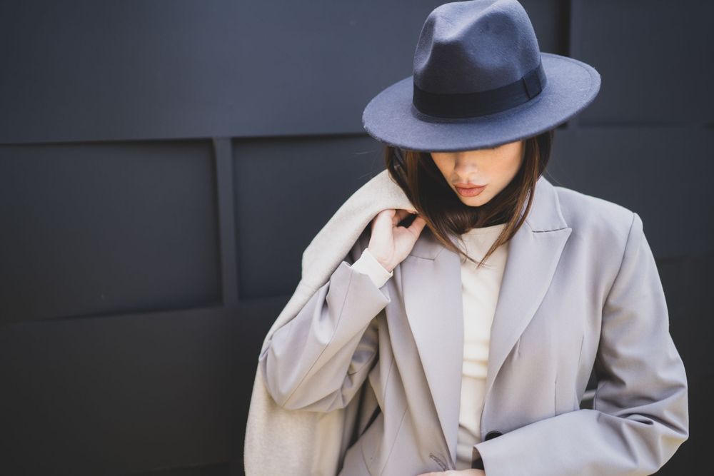 Dramatic fashion shot of model in gray coat and fedora hat.
