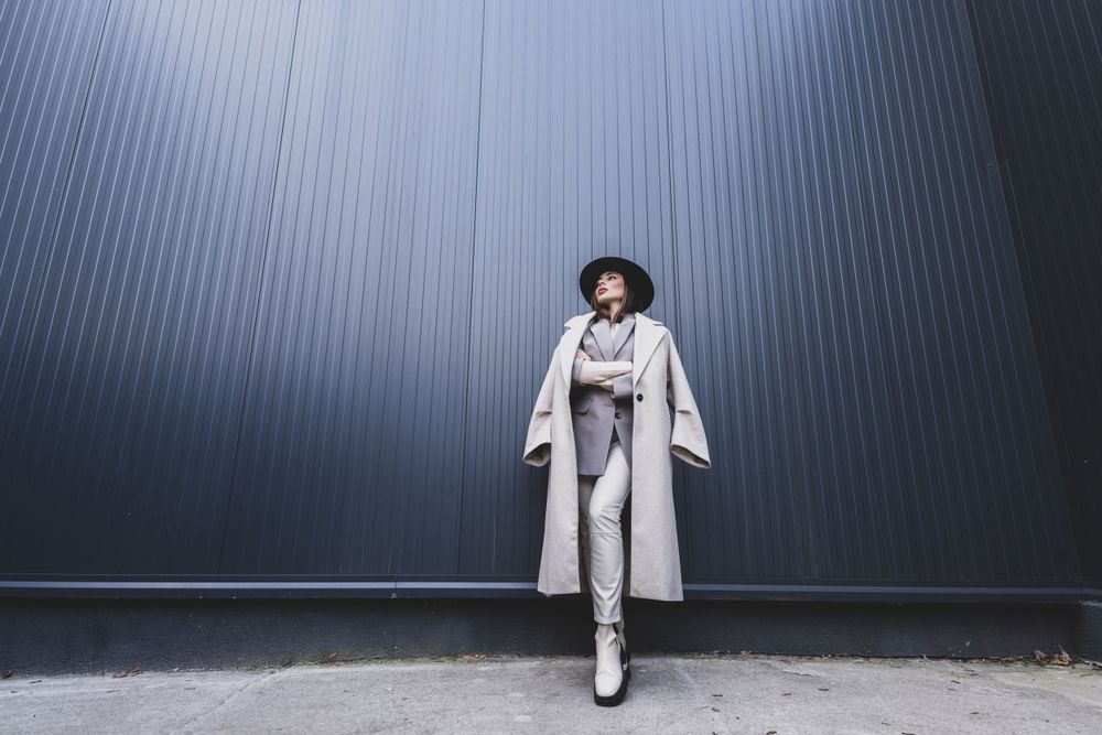 Minimalist fashion photo of model in white outfit and hat against industrial wall.