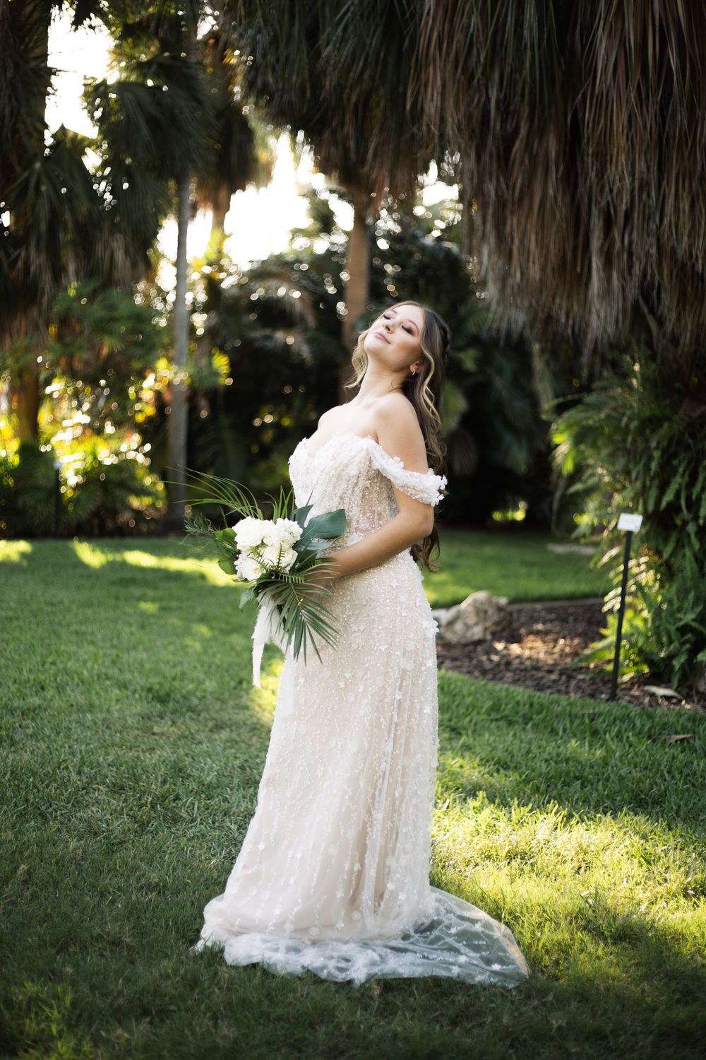Beautiful bridal portrait featuring an elegant lace gown and bouquet amidst palm trees at sunset.