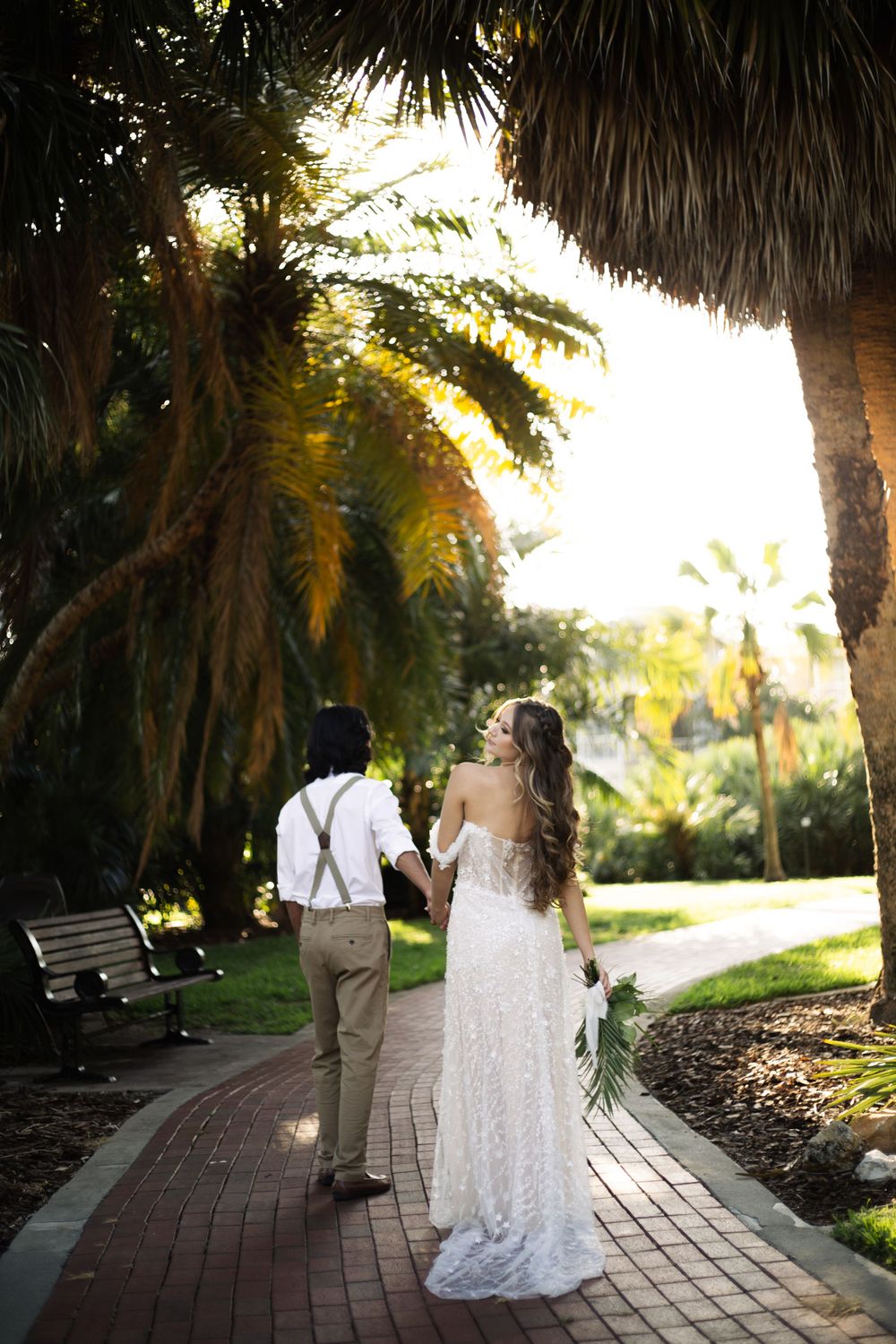 Couple walks hand in hand down a winding brick pathway surrounded by lush tropical landscaping.