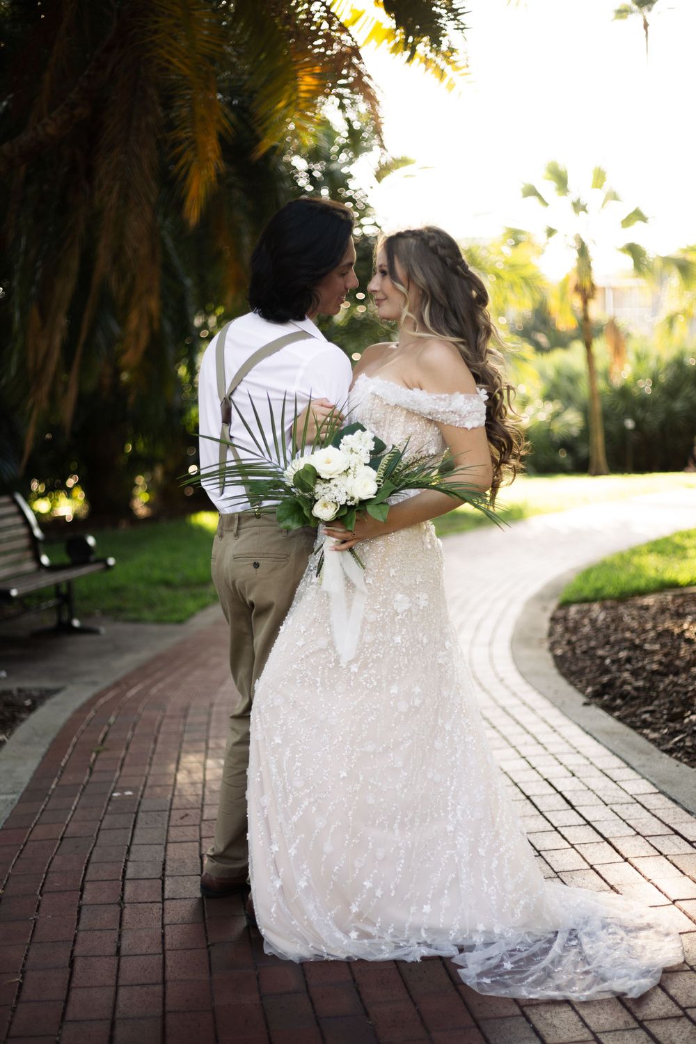 Wedding couple shares a tender moment on a garden path with palm trees overhead.