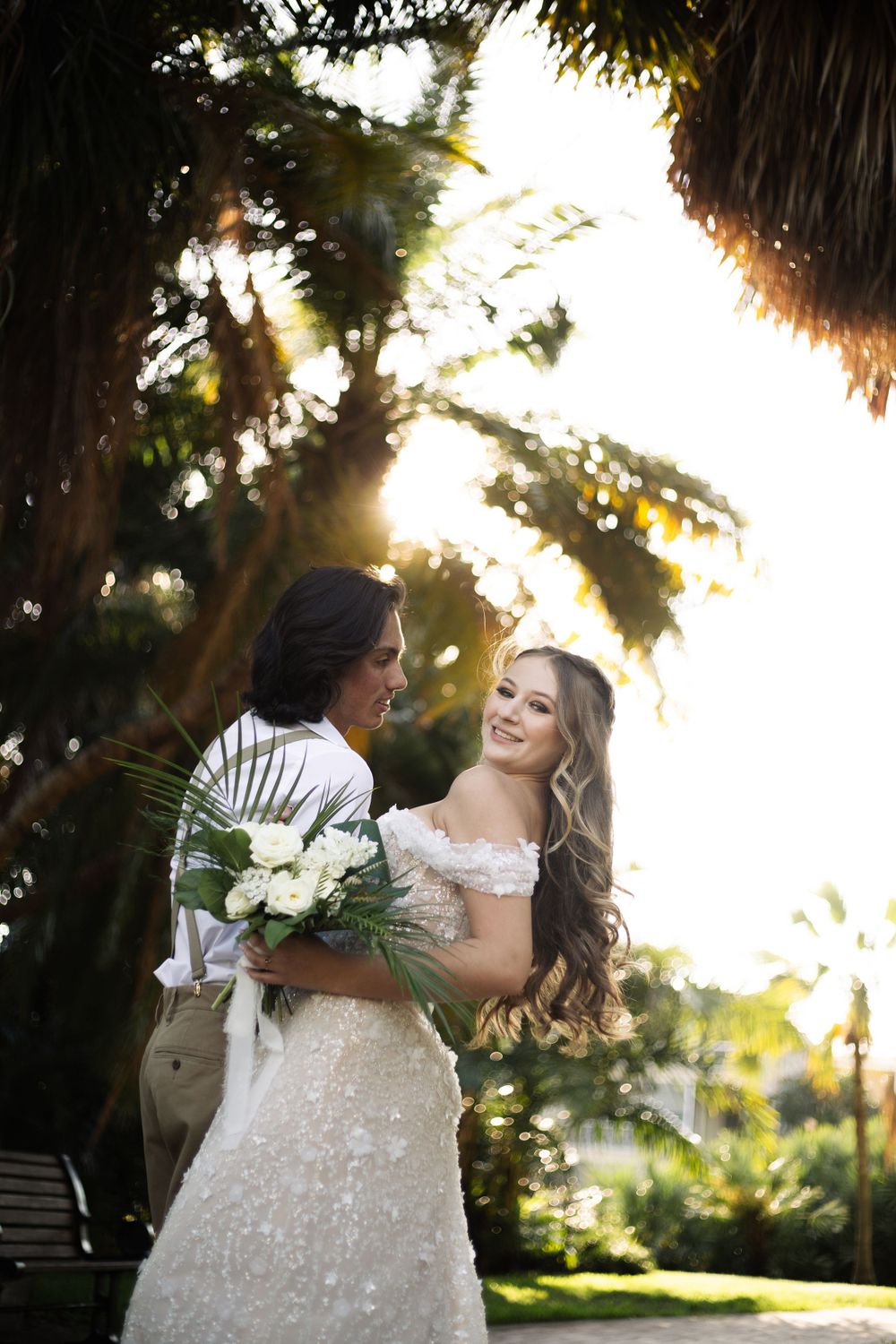 Sunlit wedding portrait capturing a joyful moment between couple under tropical palms.