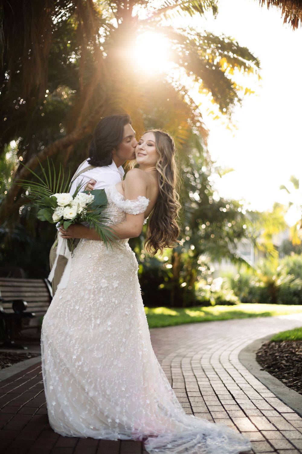 Romantic sunset embrace between newlyweds on a garden pathway with palm trees.
