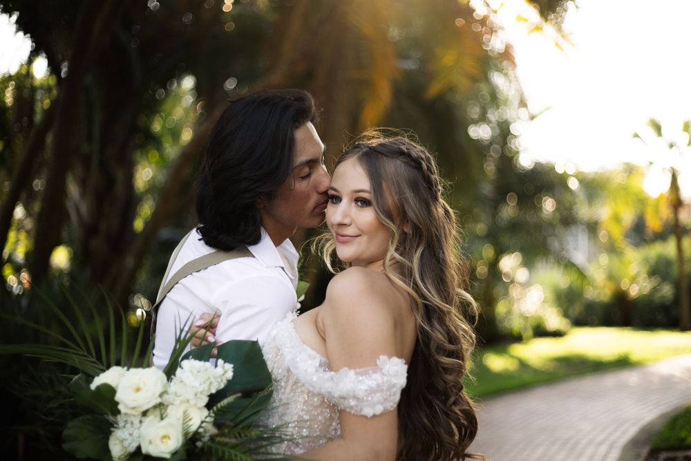 Tender moment between newlyweds captured against a tropical garden backdrop at sunset.