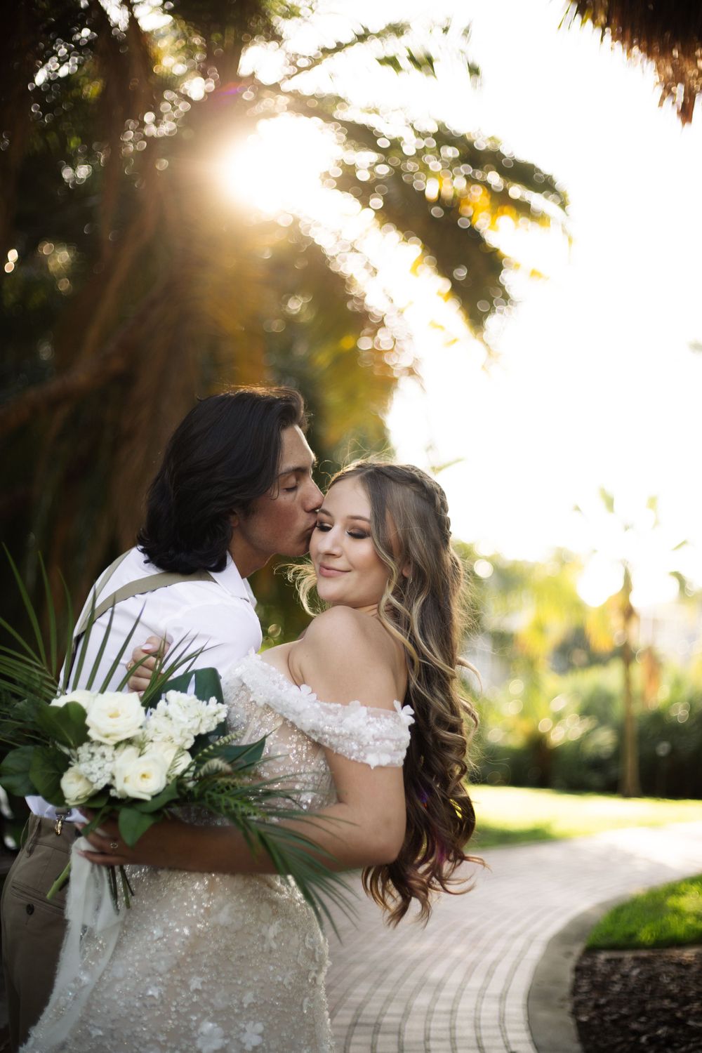 Intimate wedding moment captured on a brick path with golden sunlight filtering through palm fronds.