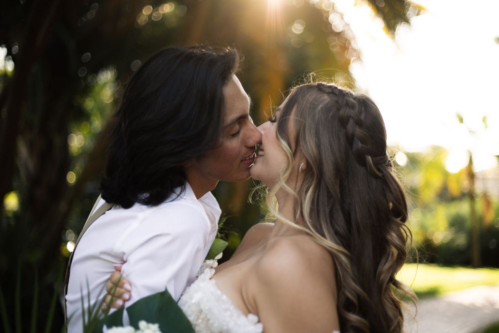 A romantic wedding kiss captured in warm sunset lighting with lush garden scenery.