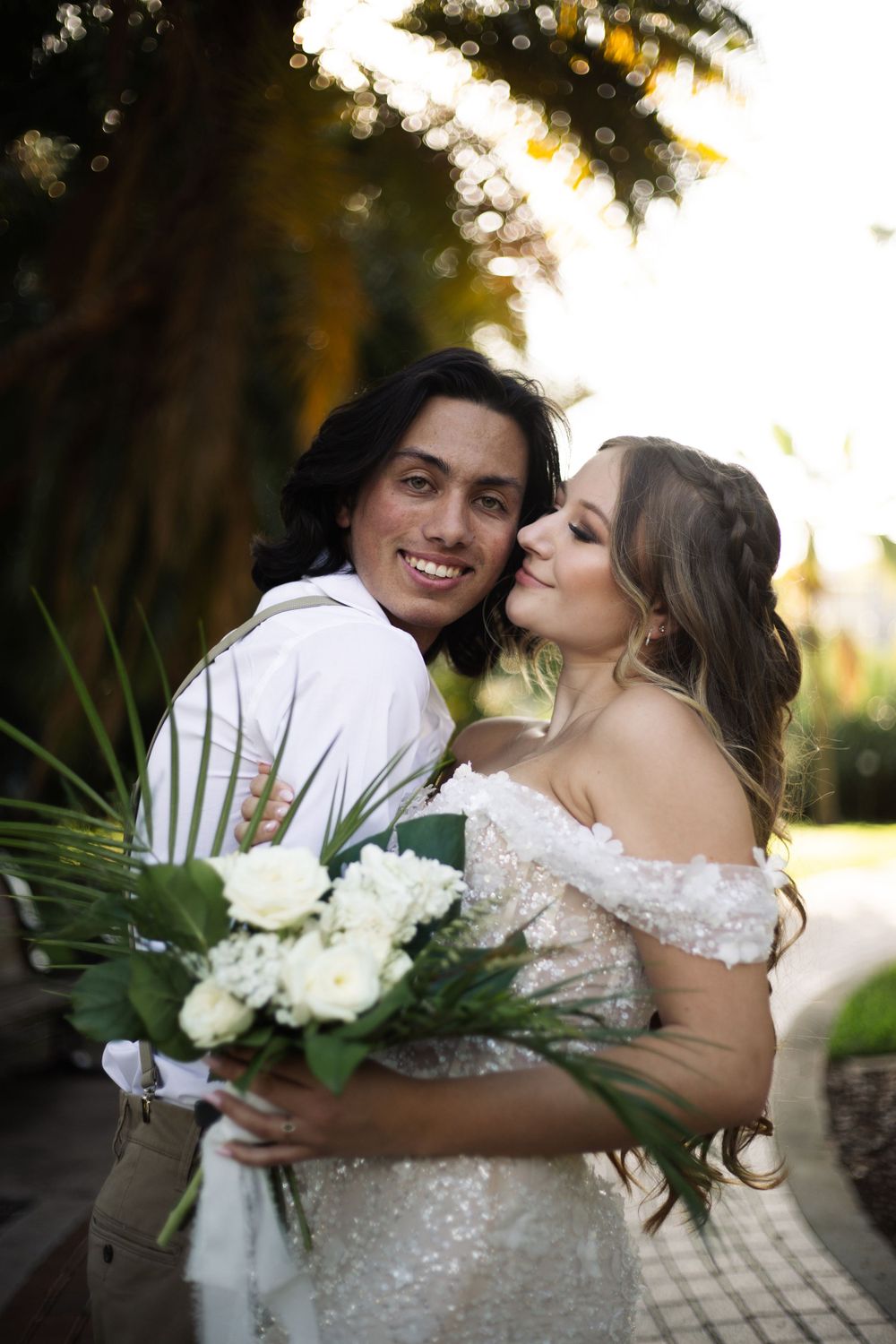 A joyful wedding couple sharing a playful moment while holding a bouquet of white flowers.