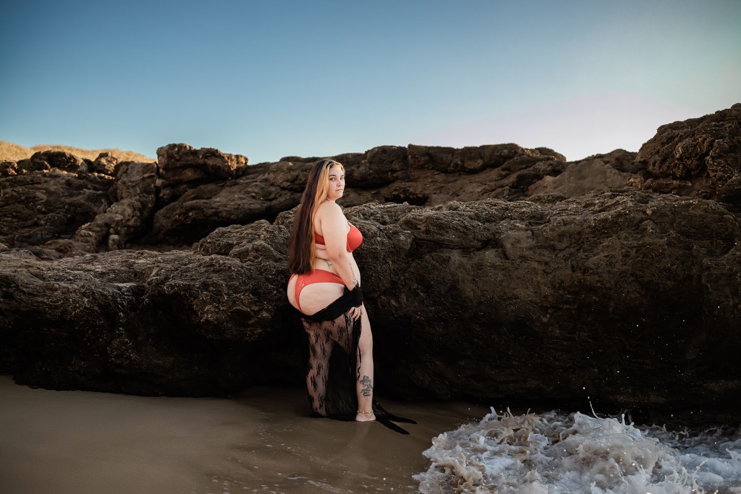 Person in orange swimsuit stands on rocky beach at sunset.