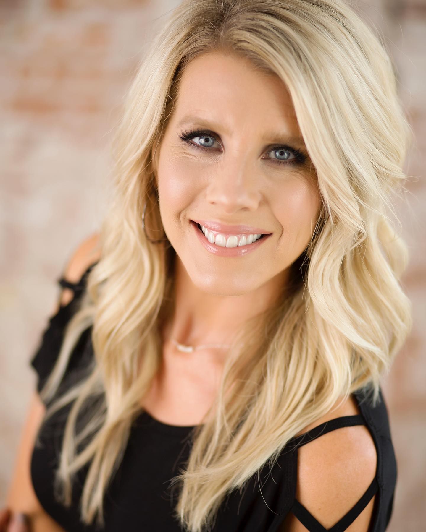 Professional headshot of a smiling woman with blonde hair wearing a black top against a blurred background.