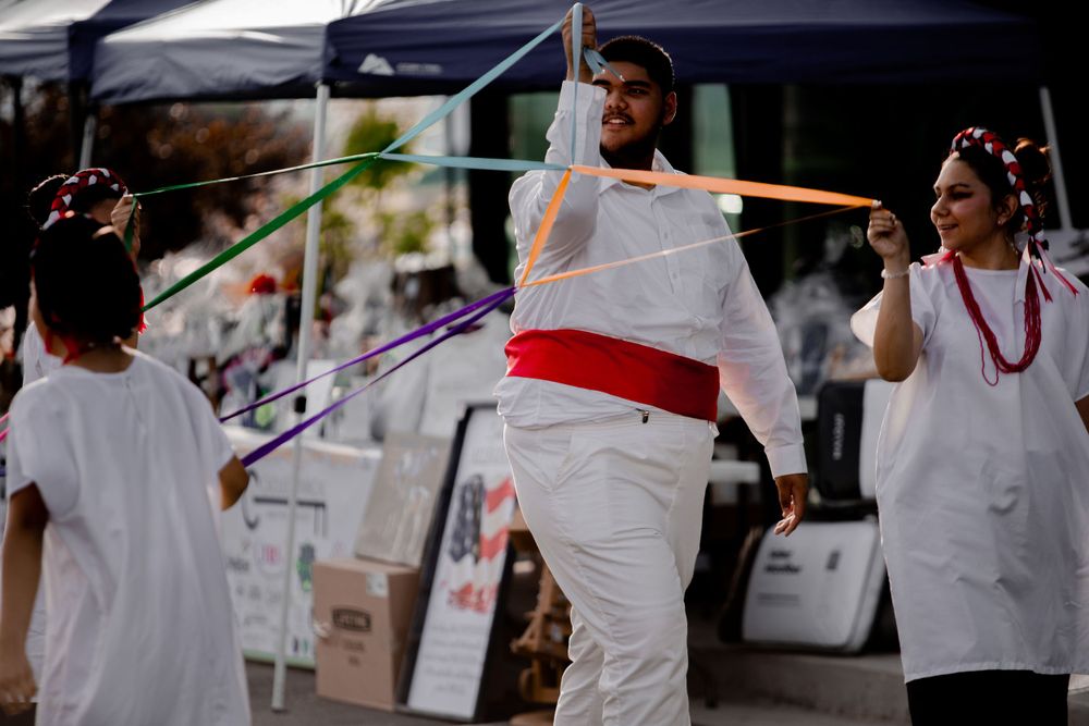 Cultural dancers in white traditional costumes performing with ribbons at an outdoor event.