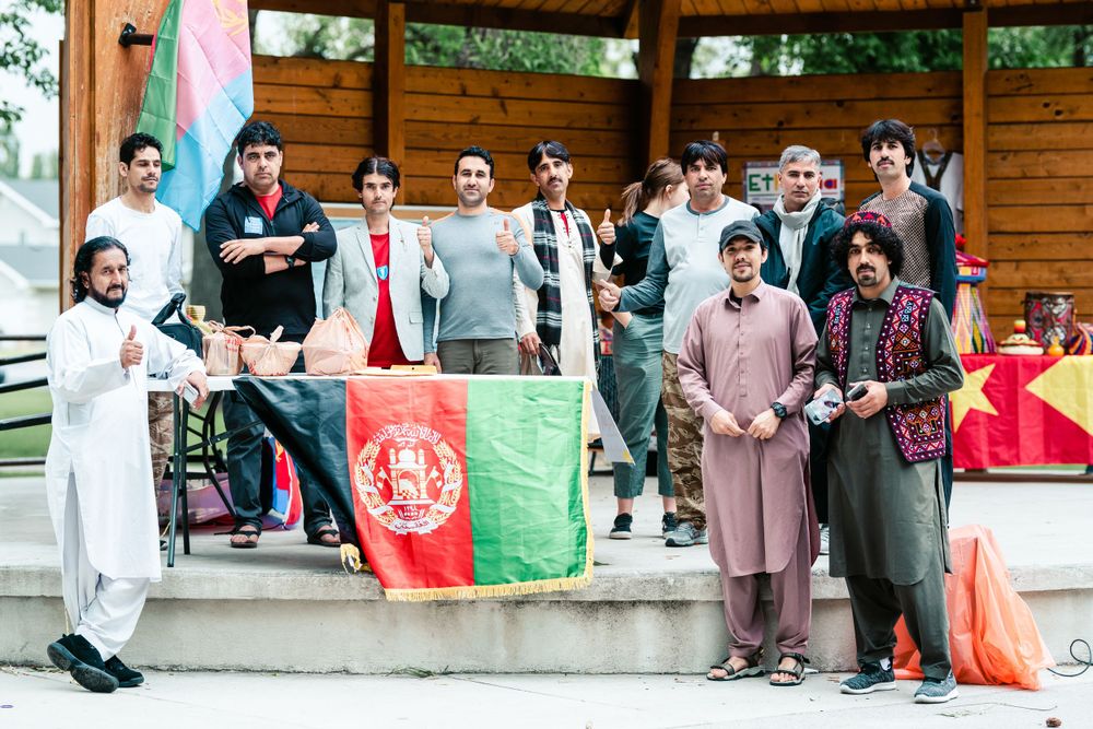 Group gathered on wooden stage with Afghanistan flag during cultural celebration event.