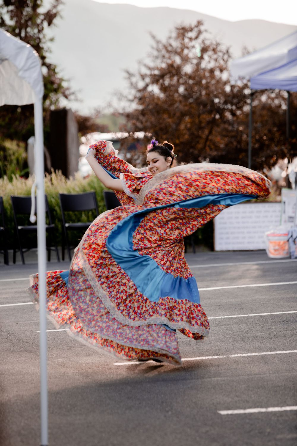 Dancer spins in a vibrant red and blue patterned dress during an outdoor cultural performance.
