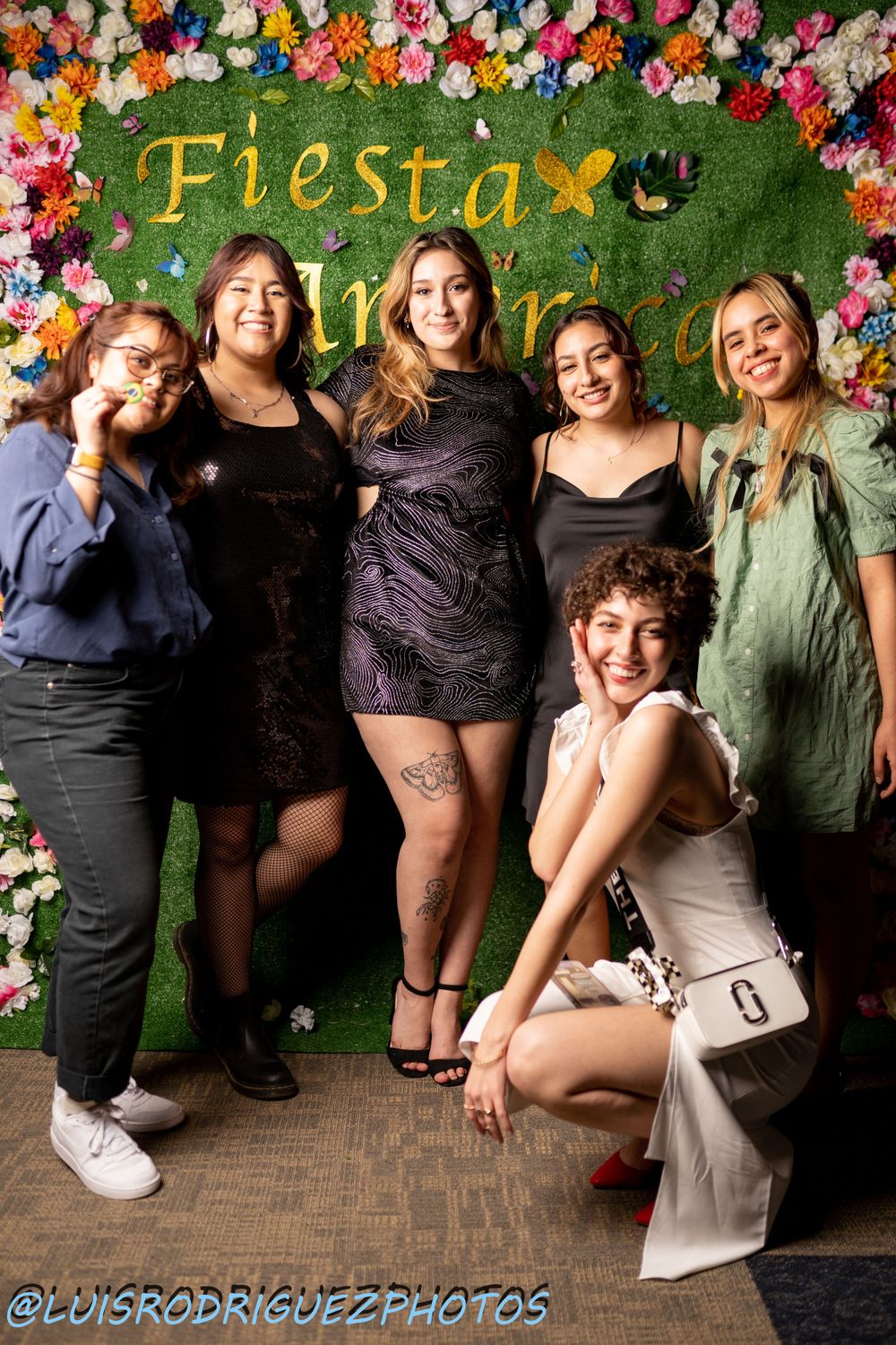 Group poses together against floral wall at festive celebration.