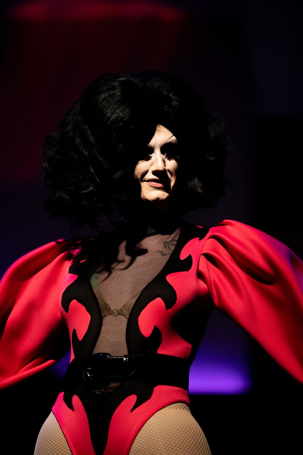Performer in striking red and black costume with dramatic styling on stage.