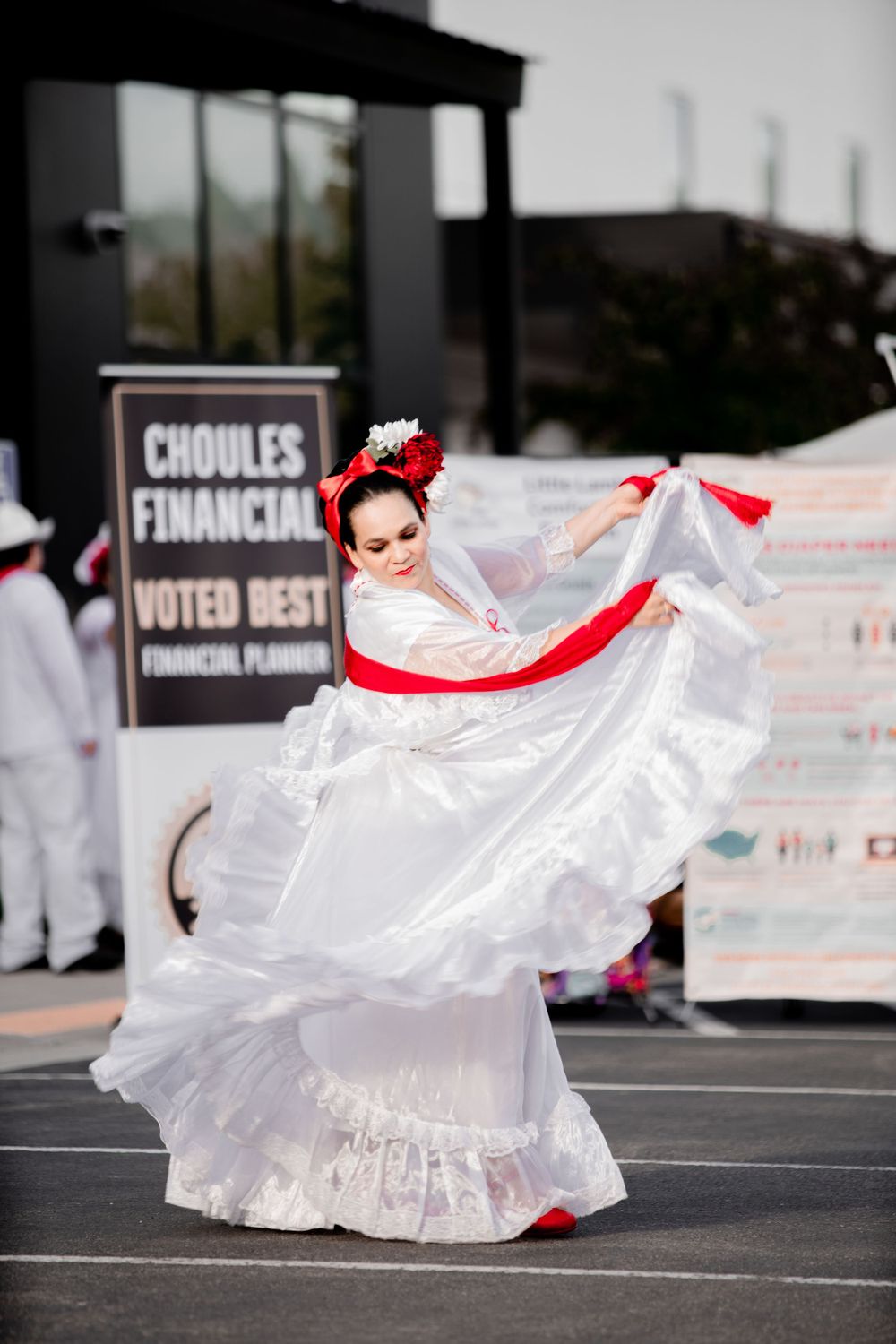 Dancer in a flowing white dress with red accents twirls gracefully during an outdoor performance.