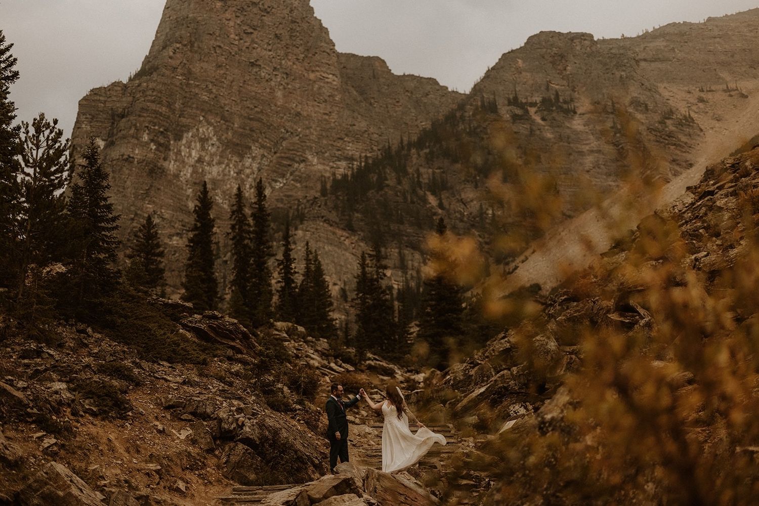 A scenic mountain landscape with rugged peaks and pine trees in golden autumn light.