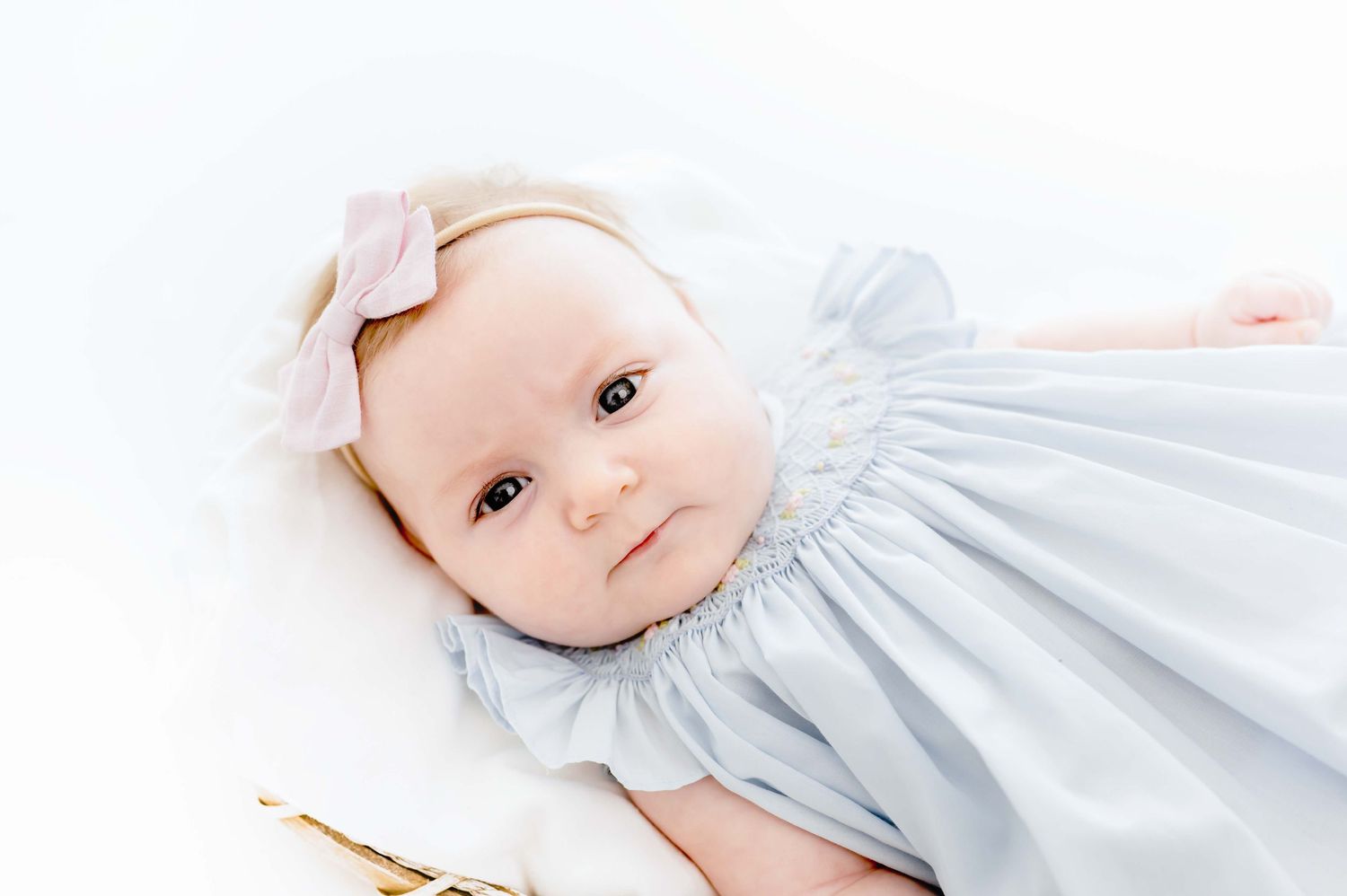 three month old wearing a light pink bow with a blue dress taking milestone portraits in an all white studio in houston