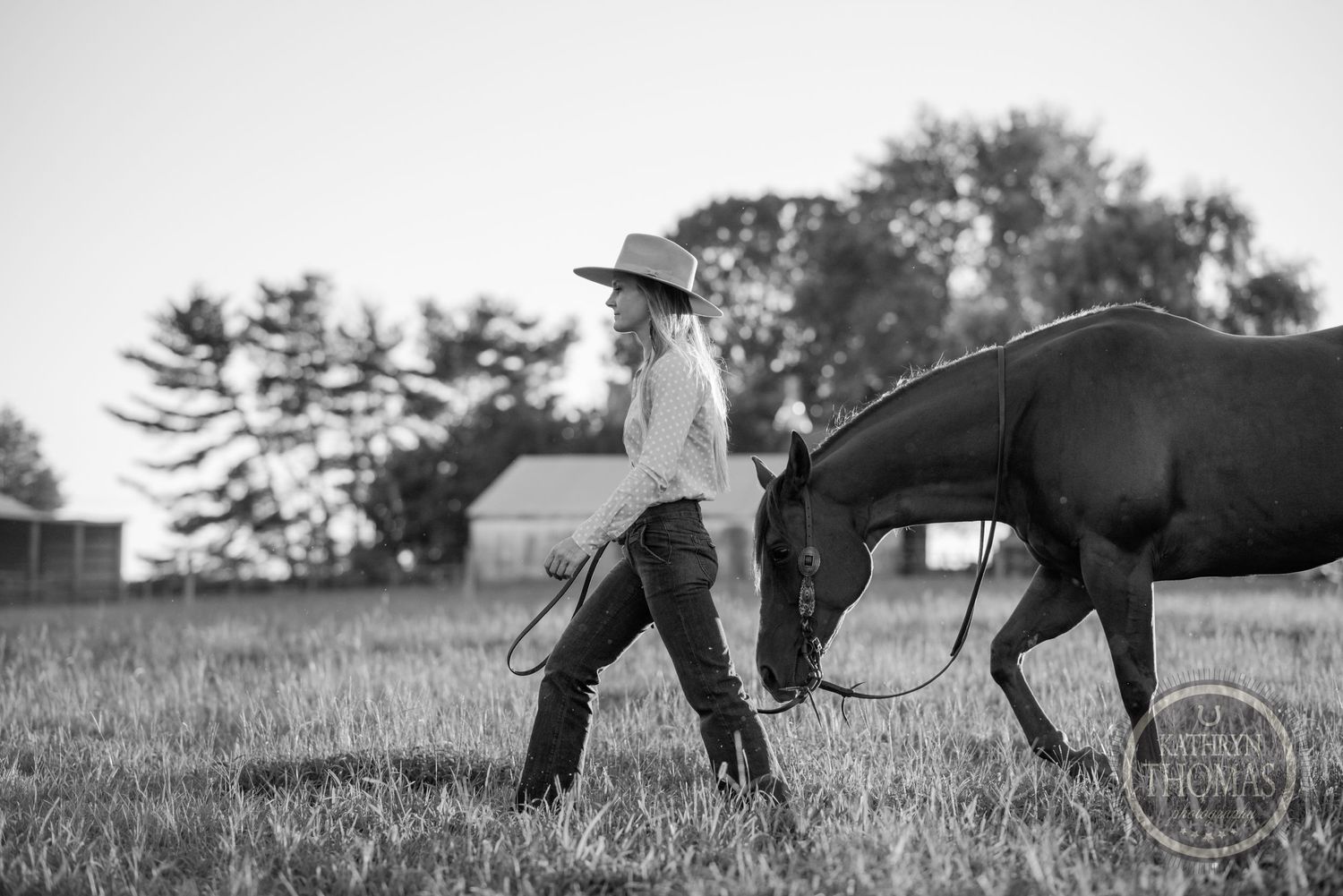 A black and white image of someone walking with a horse through a pasture.
