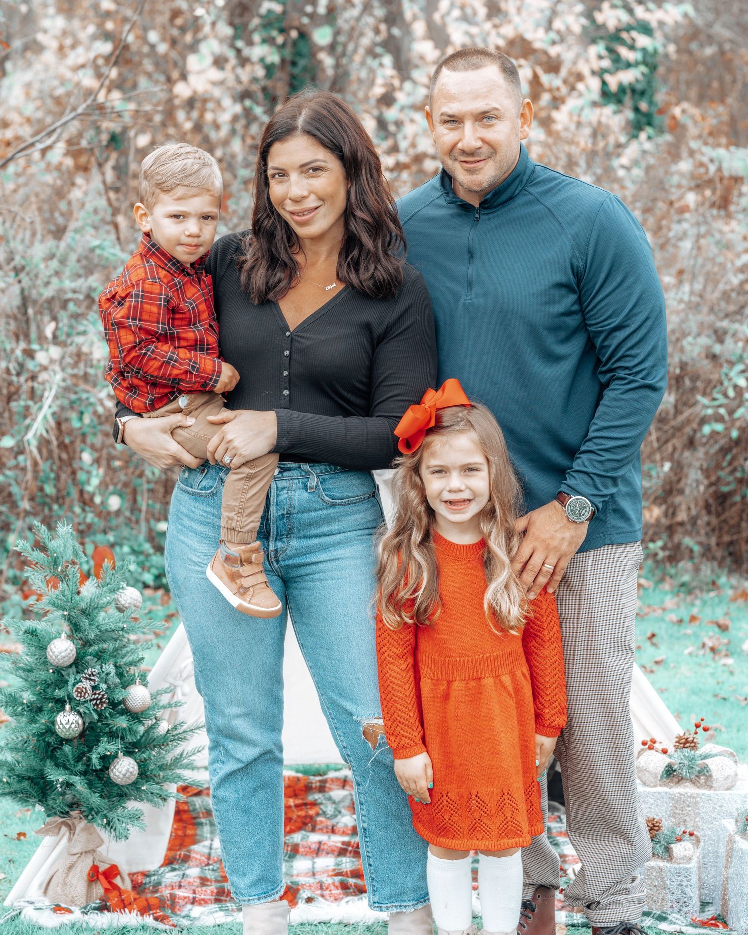 Family portrait with seasonal decor and small Christmas tree in outdoor setting.