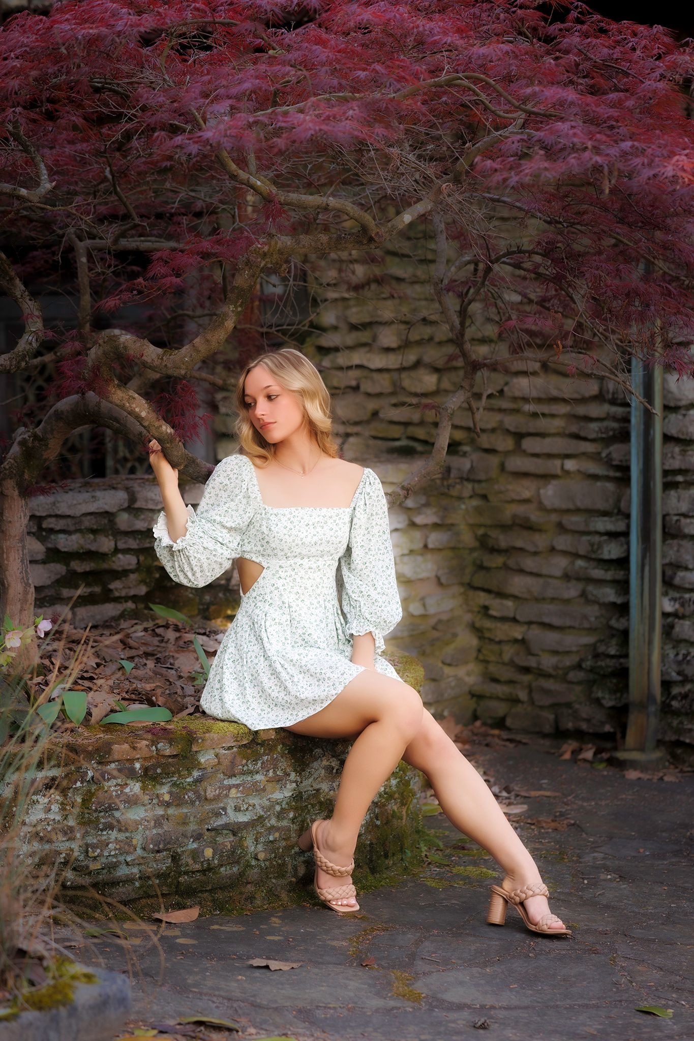 A romantic portrait in white dress against stone wall with pink flowering tree.
