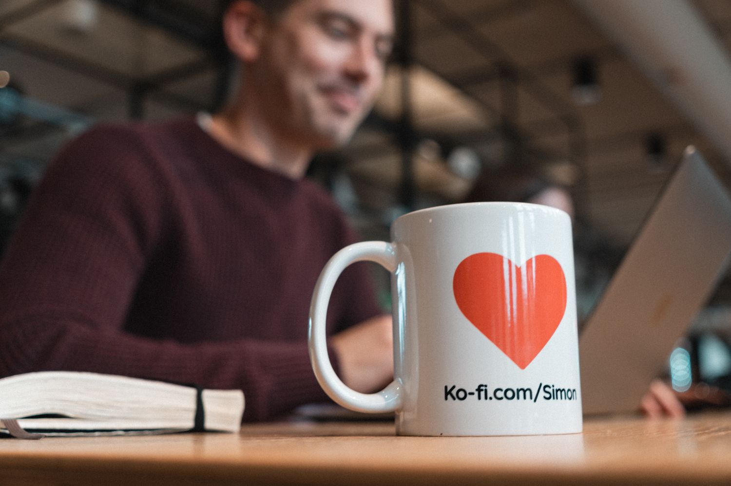coffee mug with heart branding in foreground and man in background on laptop