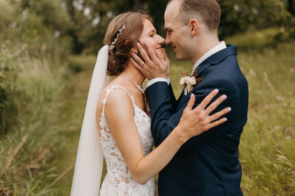 Groom tenderly holding bride's face as they smile at each other in an outdoor garden setting.