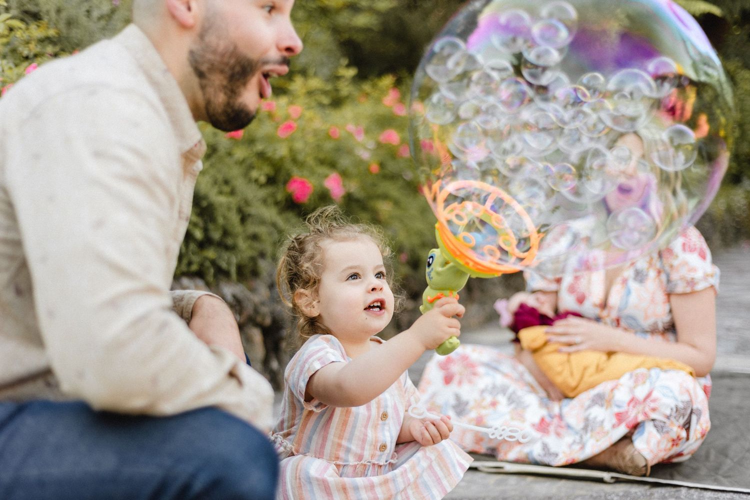 A joyful scene outdoors with bubbles floating while sitting on a blanket in a garden setting.