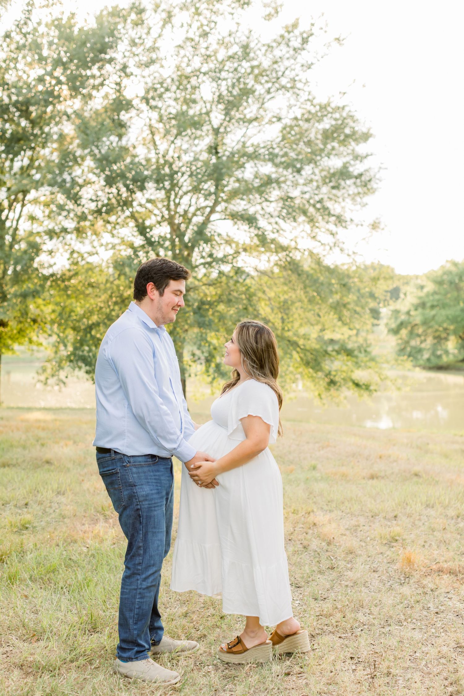 A happy couple shares a joyful moment together in a sunlit field during their maternity photoshoot.