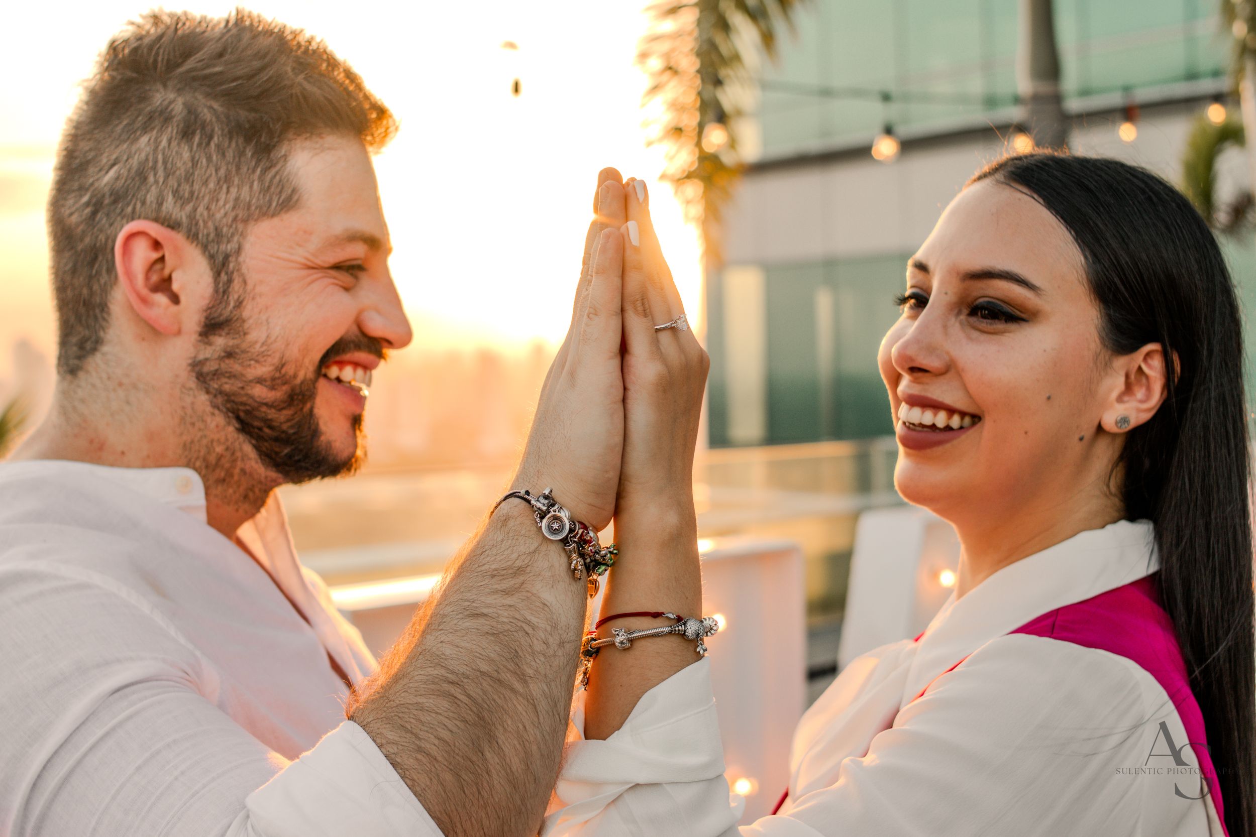Two people share a high five while smiling warmly at sunset with palm trees in the background.