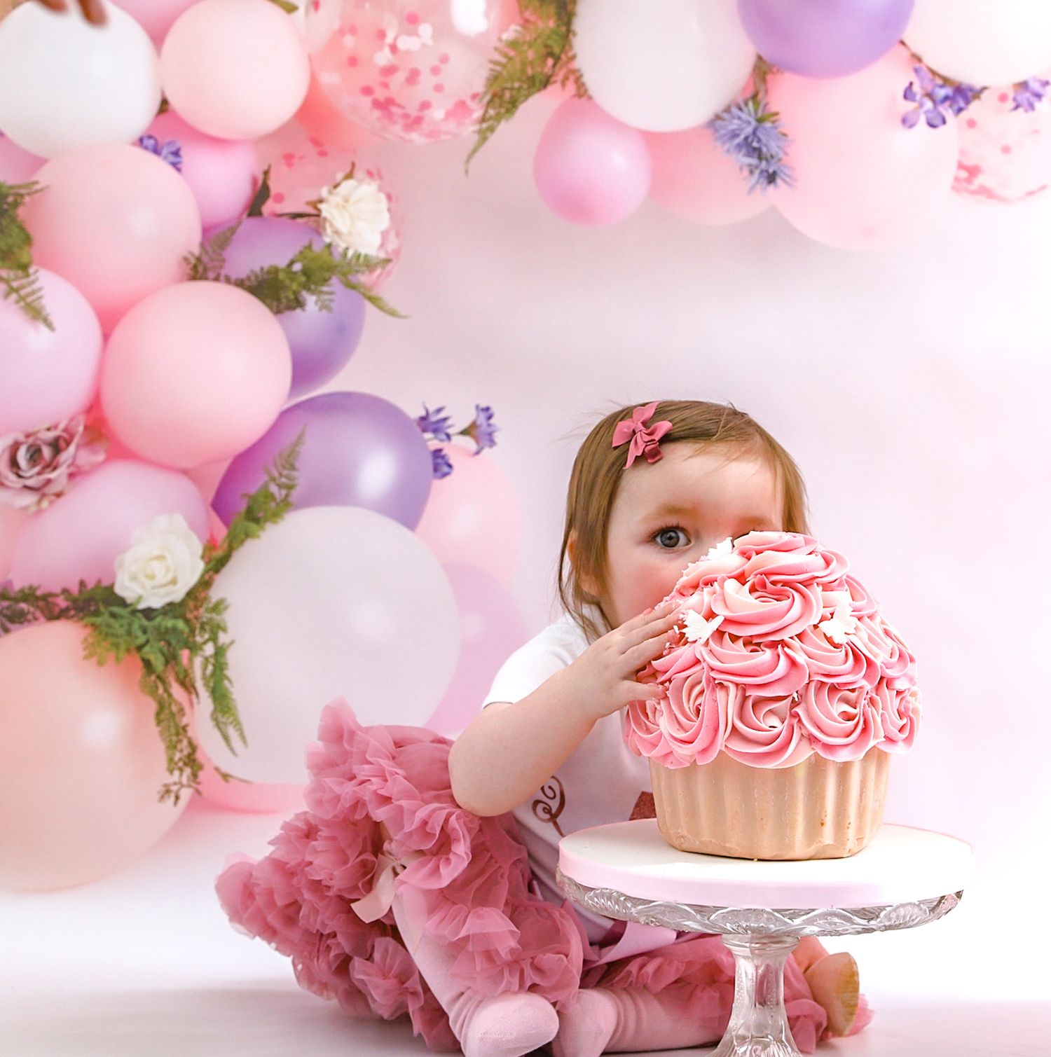 Elegant pink and purple balloon arch frames cake smash session with oversized cupcake.
