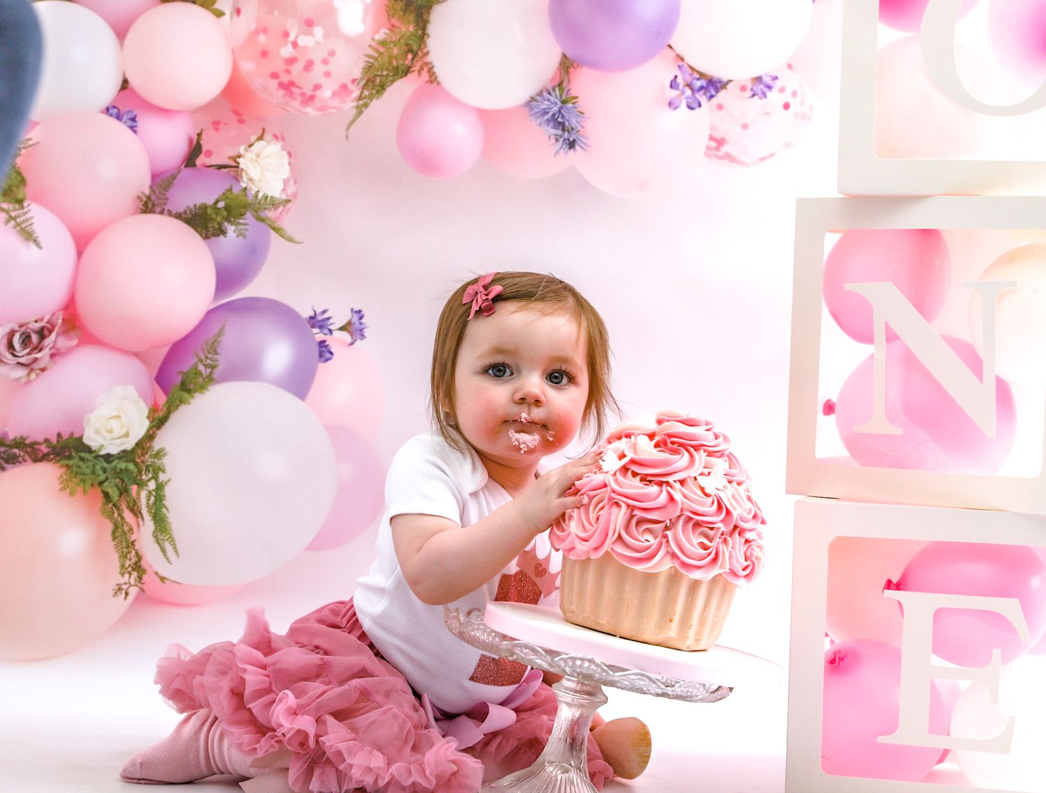 Pink and purple balloon decorated cake smash photoshoot with festive party setup.