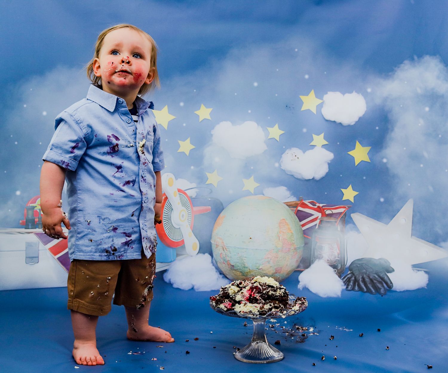Whimsical cake smash photo with globe and Union Jack flags against starry background.