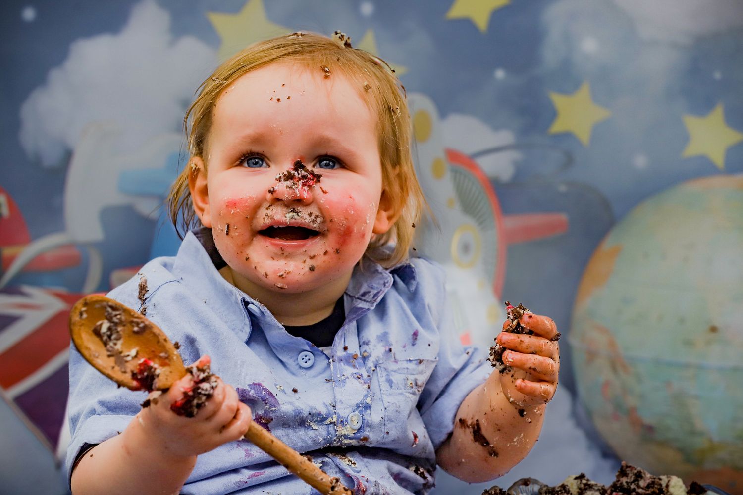 Chocolate-covered cake smash portrait with stars and globe themed backdrop.