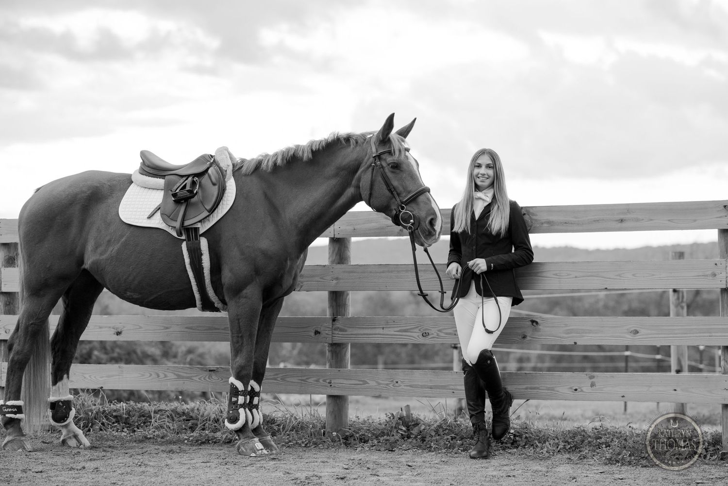 Black and white portrait of an equestrian with their horse against a rustic fence backdrop.