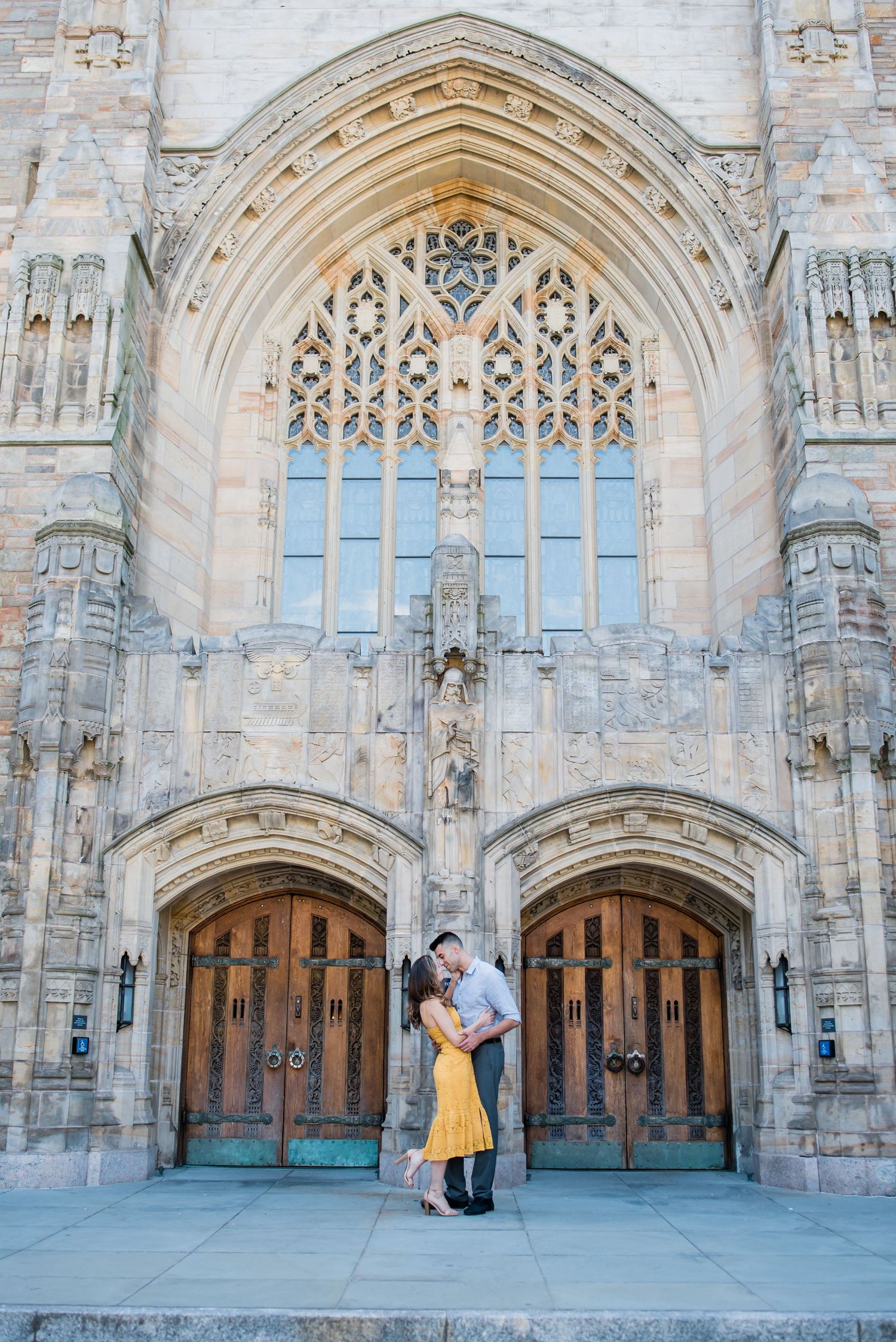 Romantic couple poses in front of Gothic cathedral entrance with ornate stone archways and stained glass.
