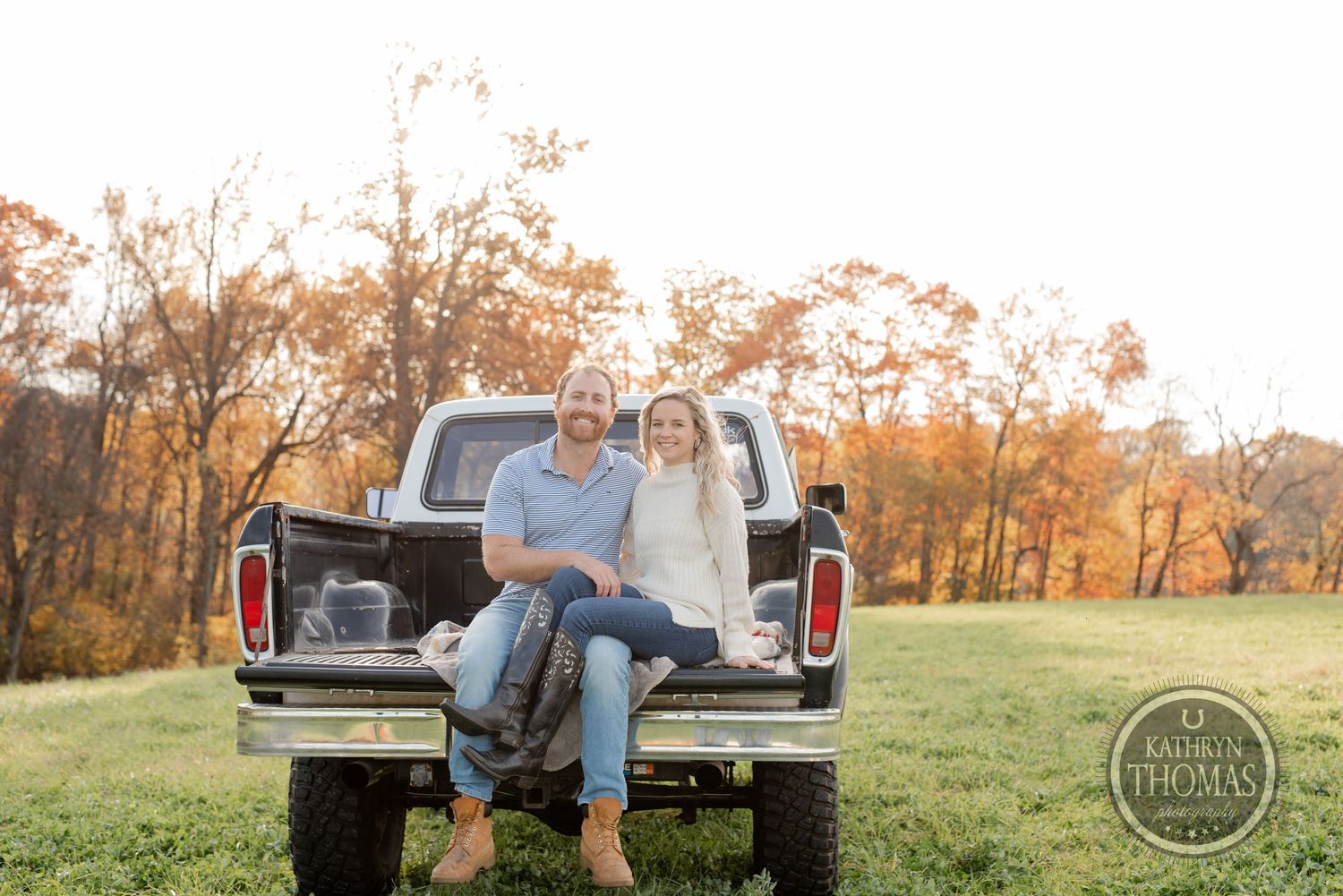 Couple sitting casually on the tailgate of a vintage pickup truck during autumn sunset.
