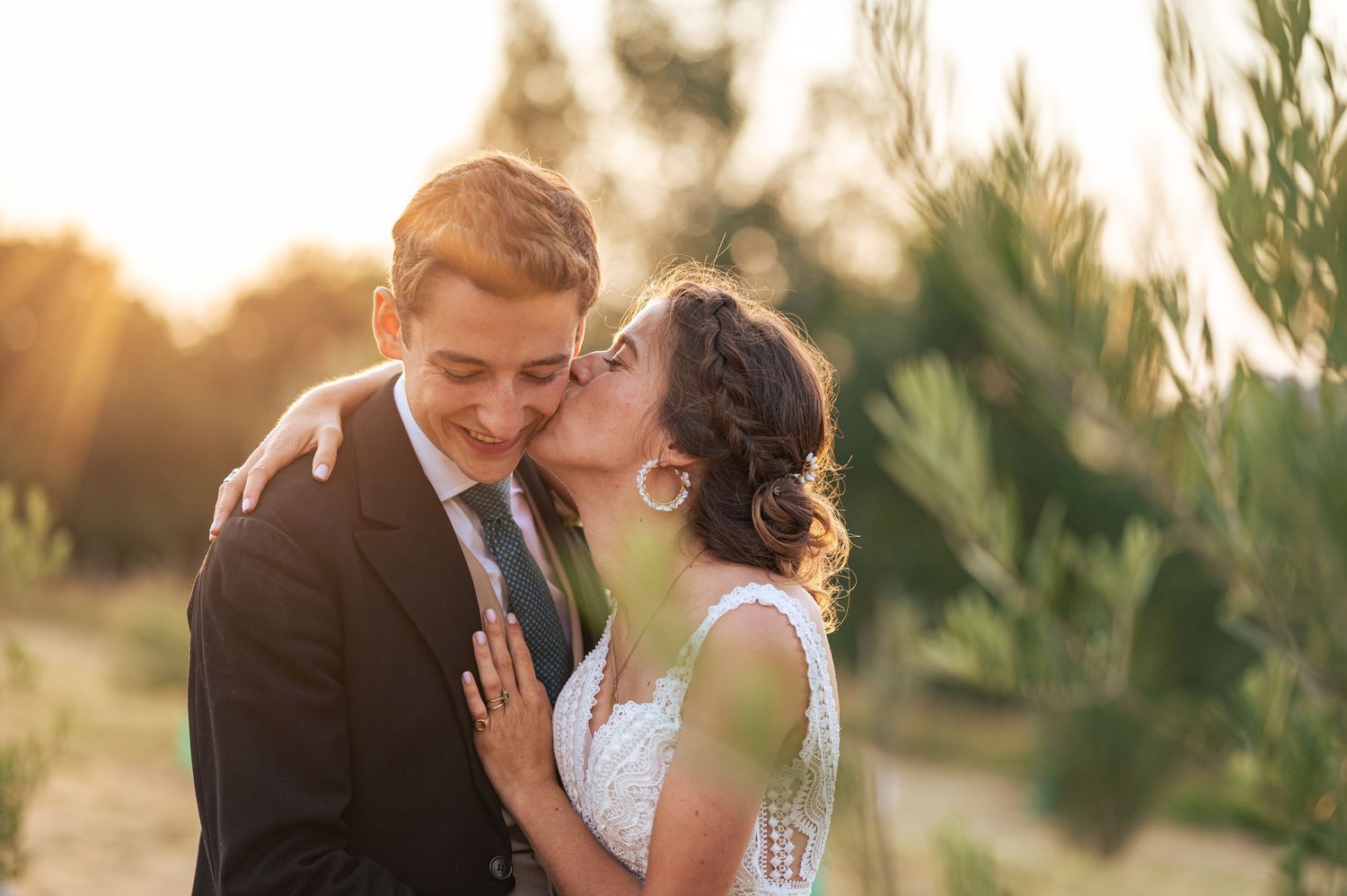 Romantic sunset wedding portrait with couple embracing in soft golden light among trees.