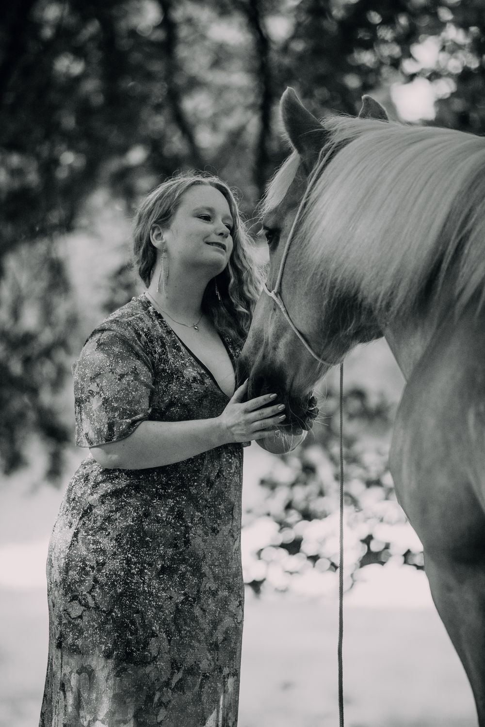 Gentle interaction between a horse and someone in a floral dress captured in monochrome.