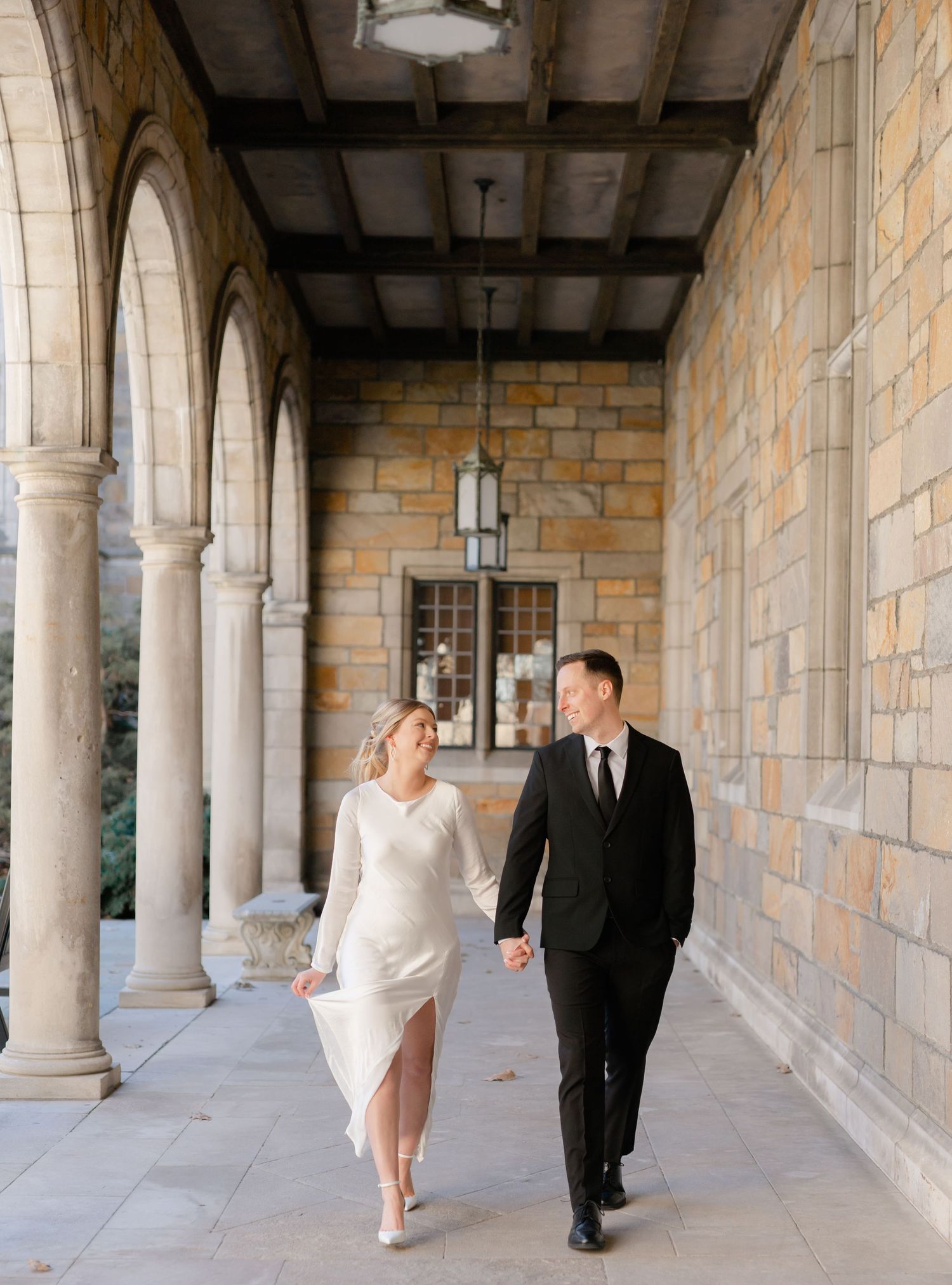A bride and groom walk together in an ornate archway. Ann Arbor Law Quad Engagement Photos