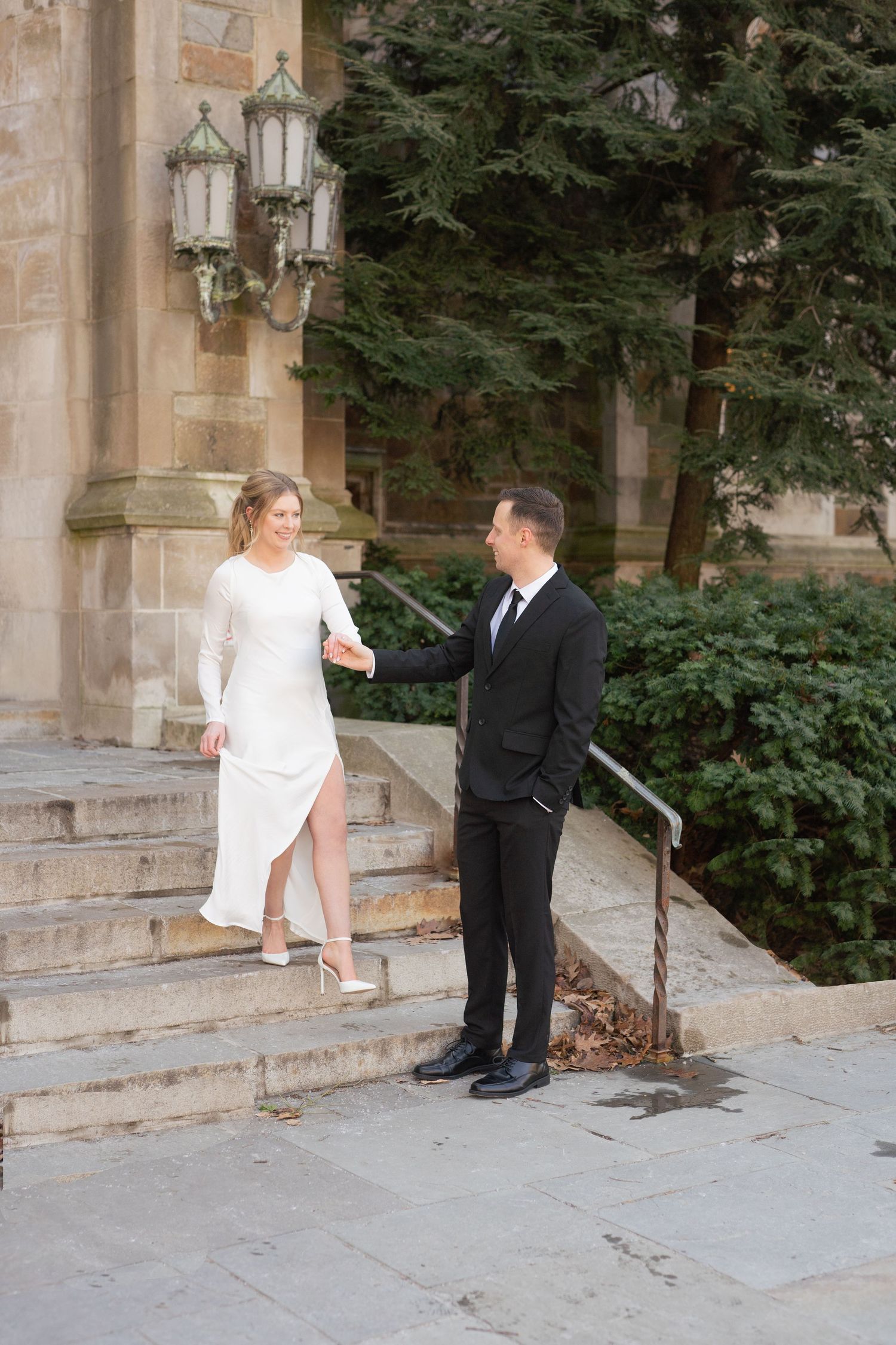 A bride and groom pose for a portrait on the steps of a building. Ann Arbor Law Quad Engagement Photos