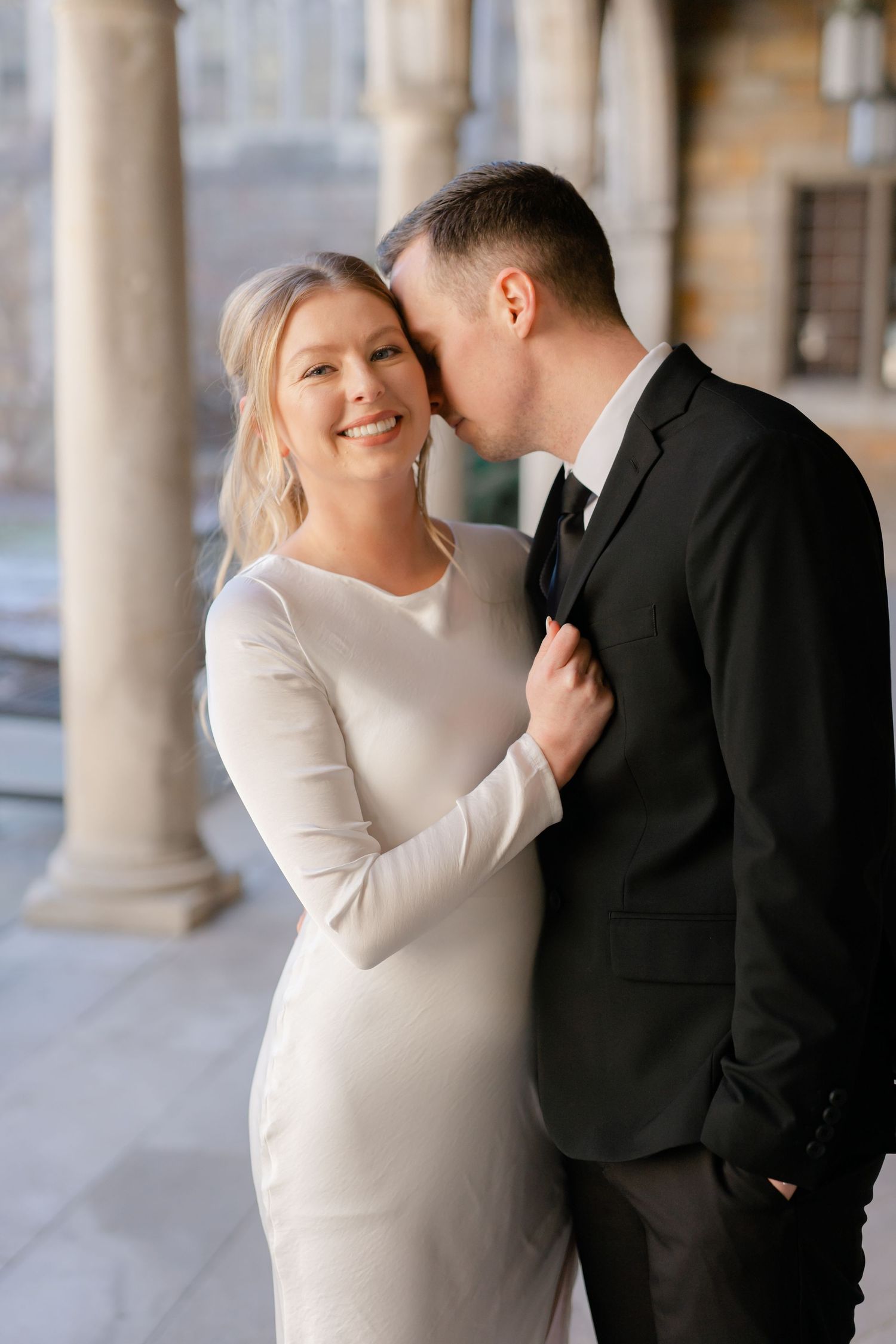 A bride and groom stand close together and smile at the camera. Ann Arbor Law Quad Engagement Photos