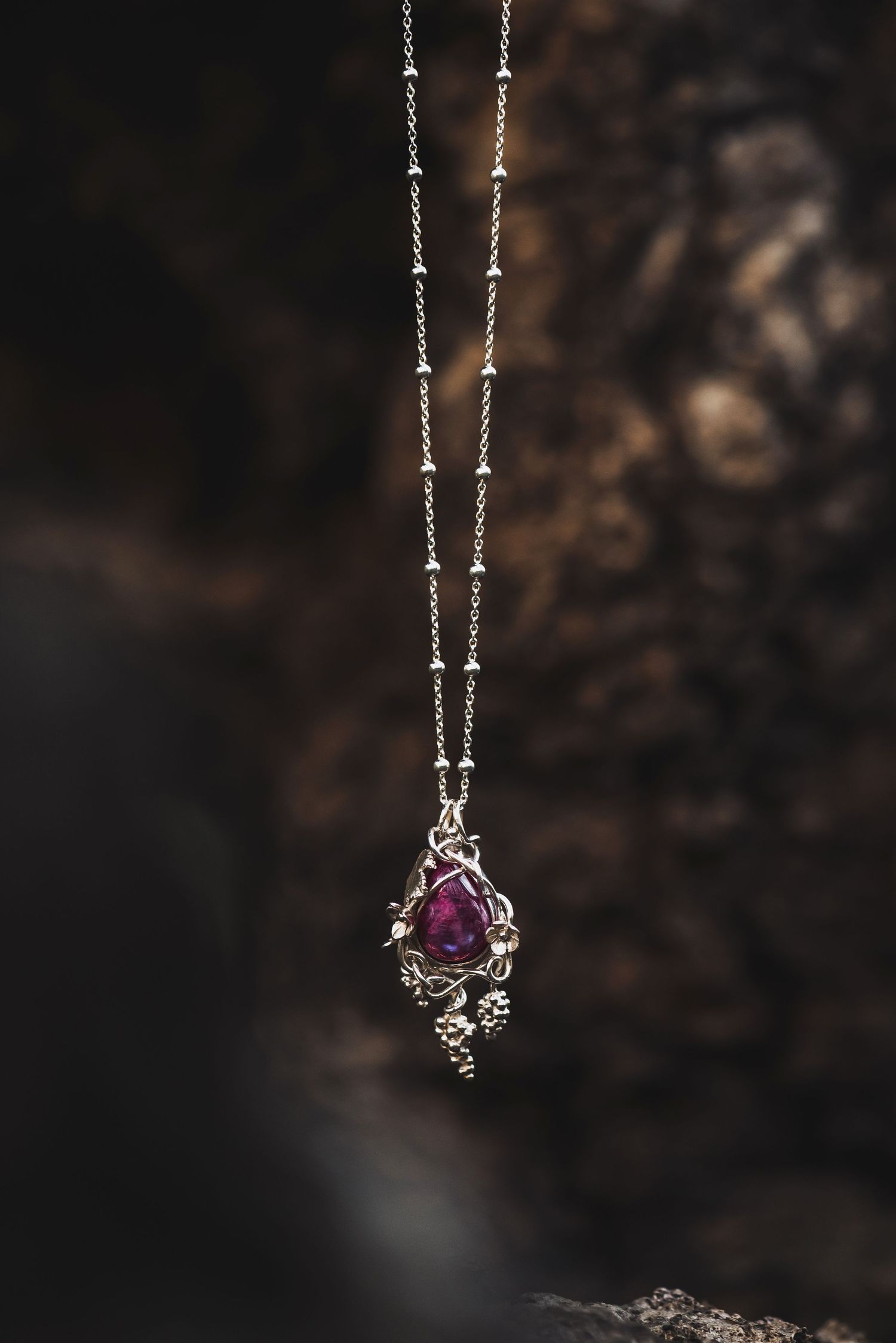 Vintage-style silver necklace with purple gemstone pendant photographed against dark background.