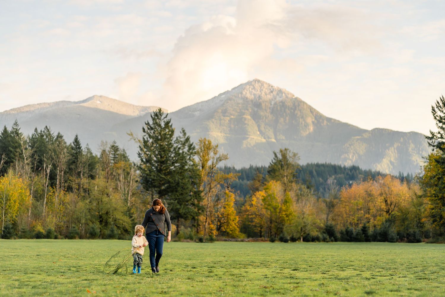 Mother holding son as they walk through a field with a mountain backdrop in North Bend.